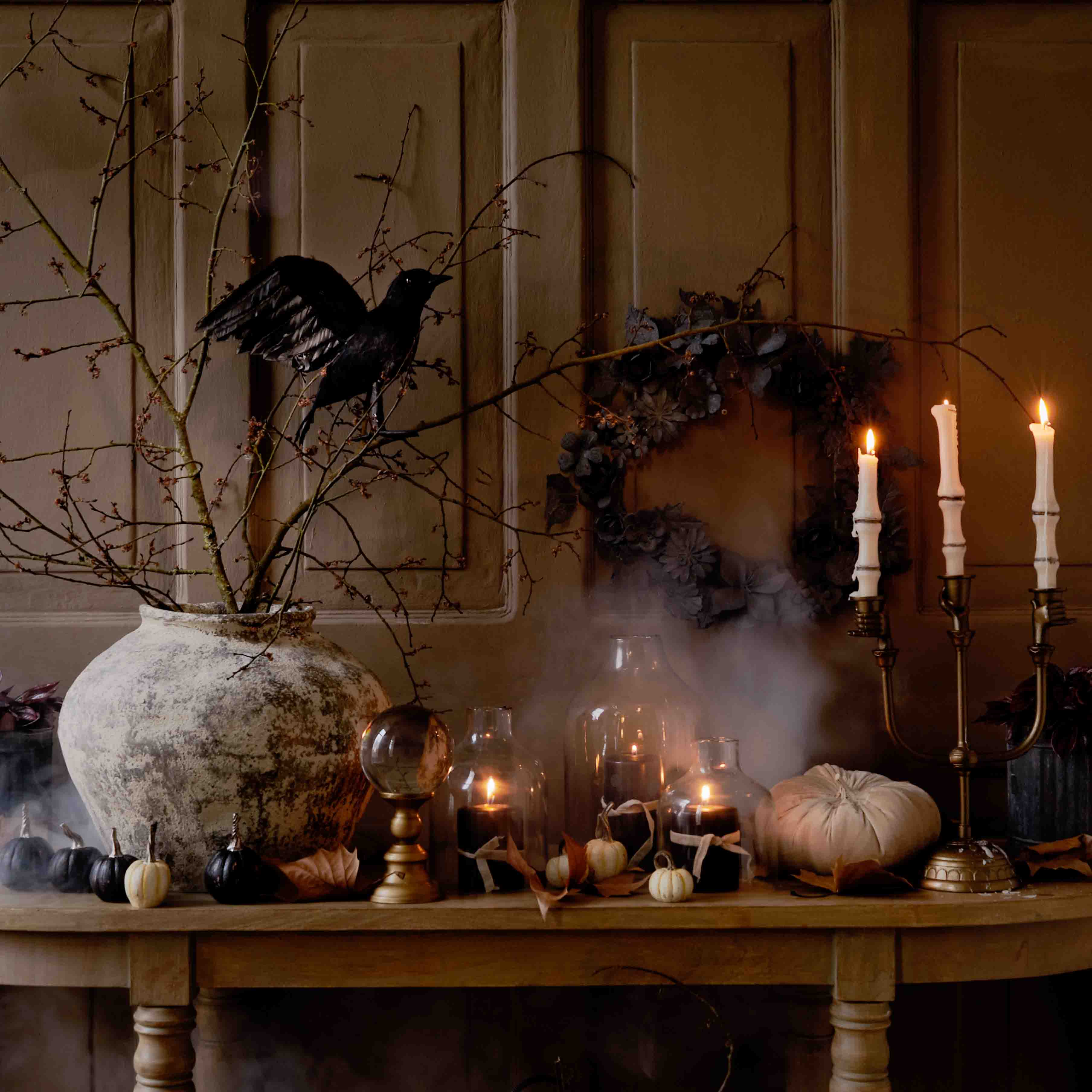 Herbstliche Tischdekoration mit großem Keramikvase, brennenden Kerzen und schwarzem Vogel auf Zweig