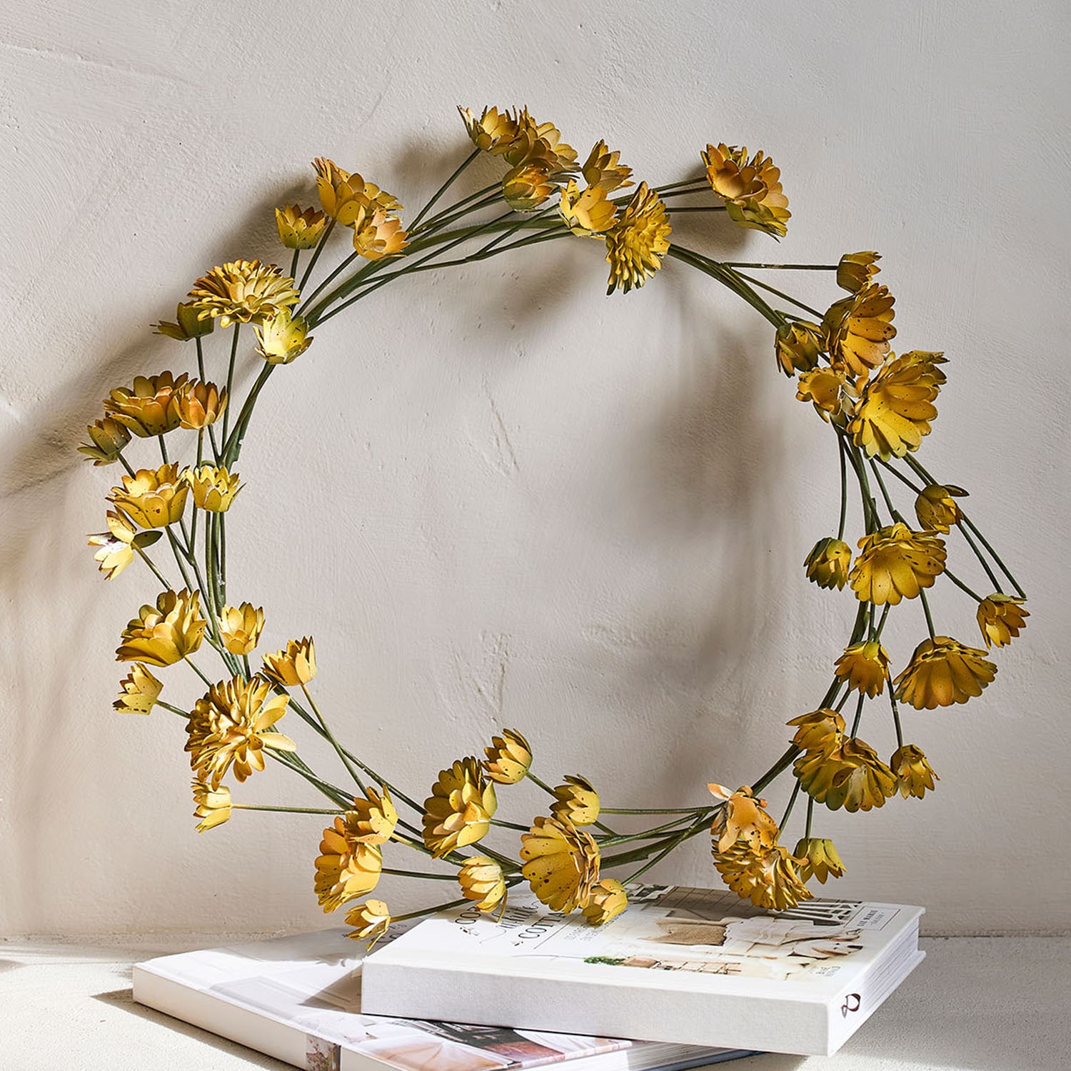 Dekorativer Kranz aus gelben Metallblumen mit grünen Stielen auf Büchern als Tischdeko