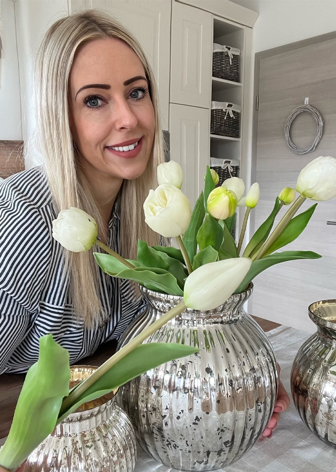 Frau mit blonden Haaren neben silberner Vase mit weißen Tulpen in modernem Interieur