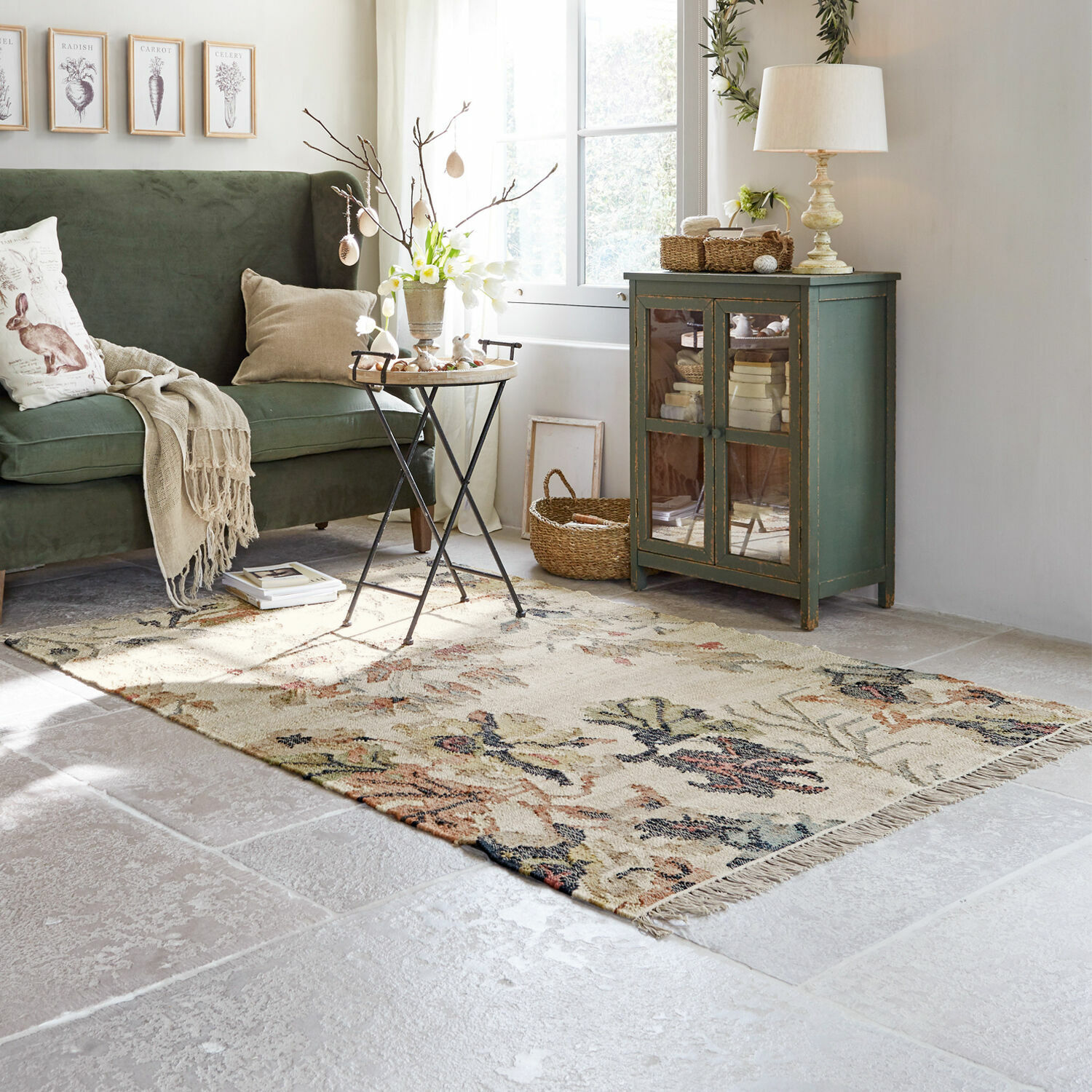 Gemütliches Wohnzimmer mit grünem Sofa, beigem Blumenmuster-Teppich und vintage Holzschrank