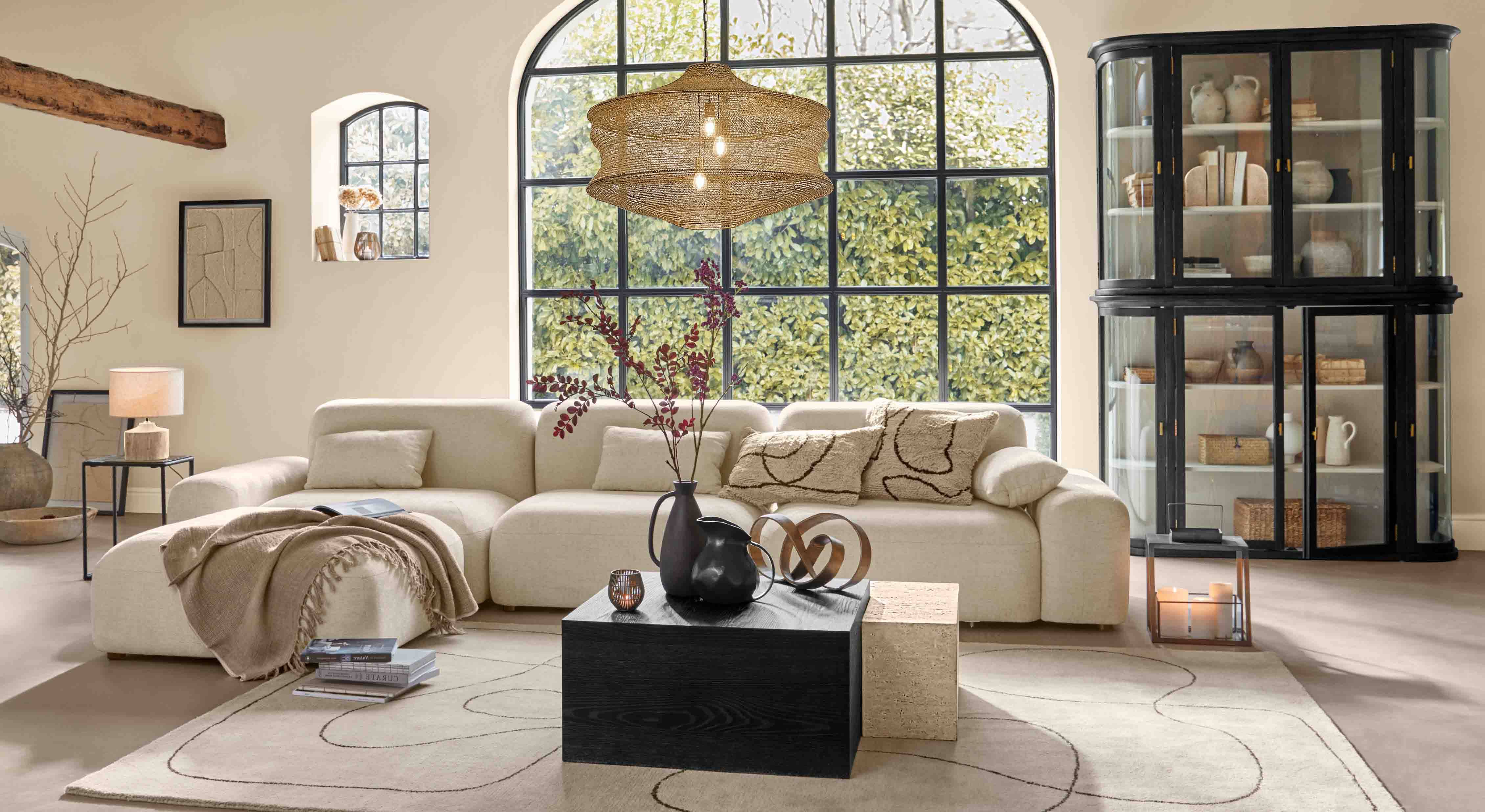 Gemütliches Wohnzimmer mit beigem Sofa, schwarzem Schrank und großem Fenster, moderne Beleuchtung