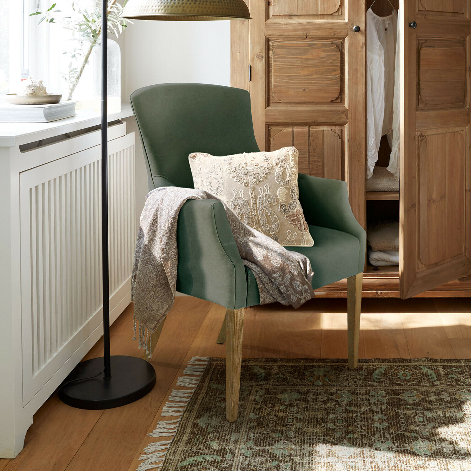 Sessel Hallmere Grüner Sessel mit Holzbeinen, cremefarbenem Kissen und grauem Plaid in gemütlichem Raum mit Holzschrank