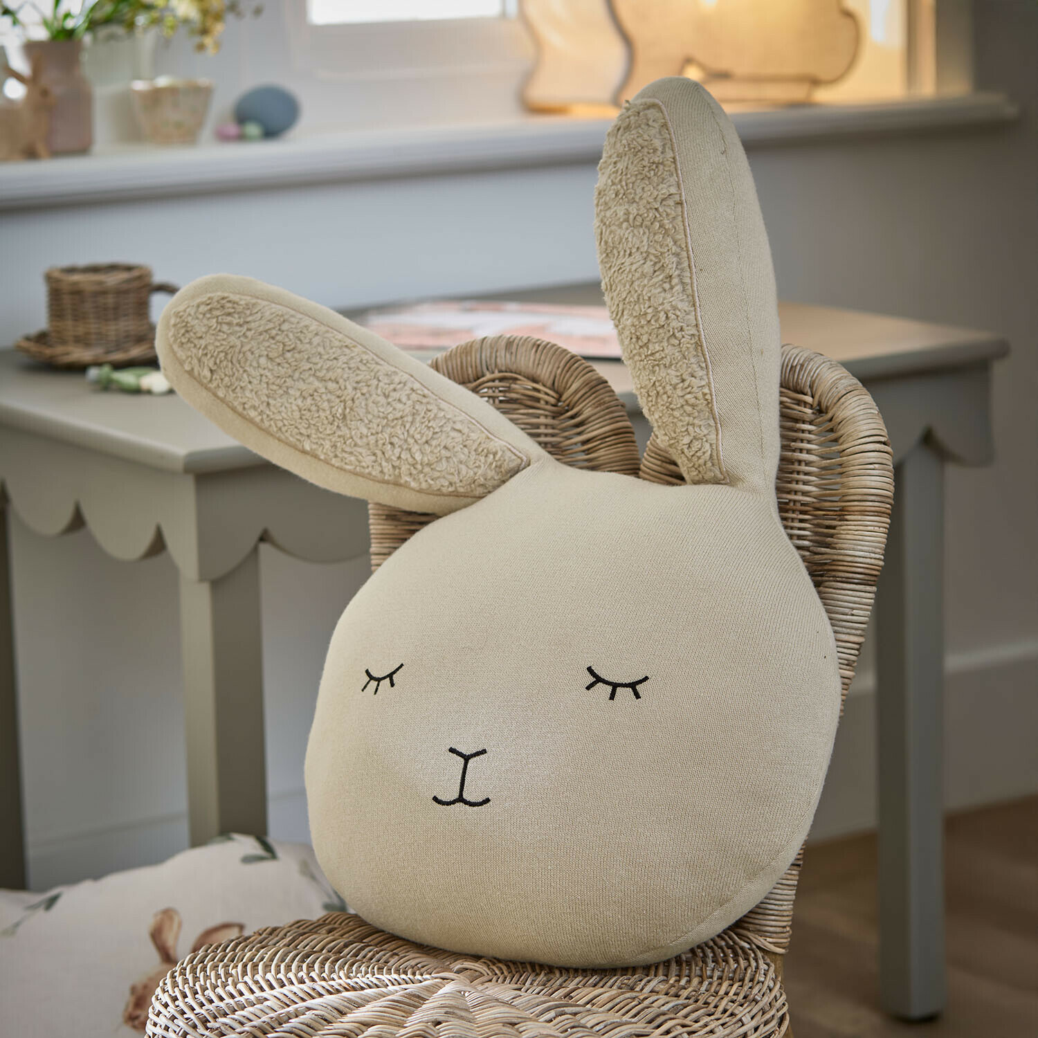 Kissen Fuzzletop Beige Hasenkissen aus weichem Stoff auf einem Rattanstuhl im Kinderzimmer