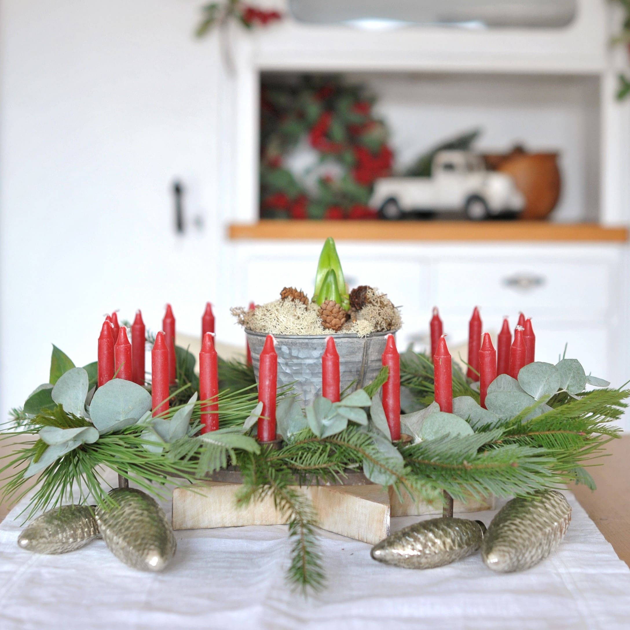 Dekorativer Adventskranz mit roten Kerzen, grünen Zweigen und metallischen Zapfen auf dem Tisch
