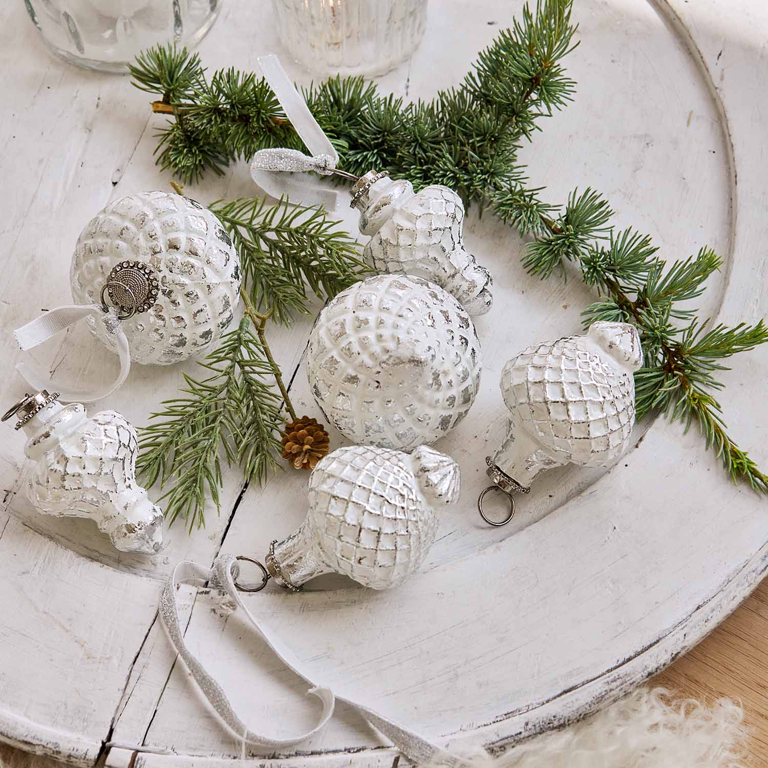 Weiße Weihnachtskugeln mit Rautenmuster auf Holztablett mit Tannenzweigen, festliche Dekoration