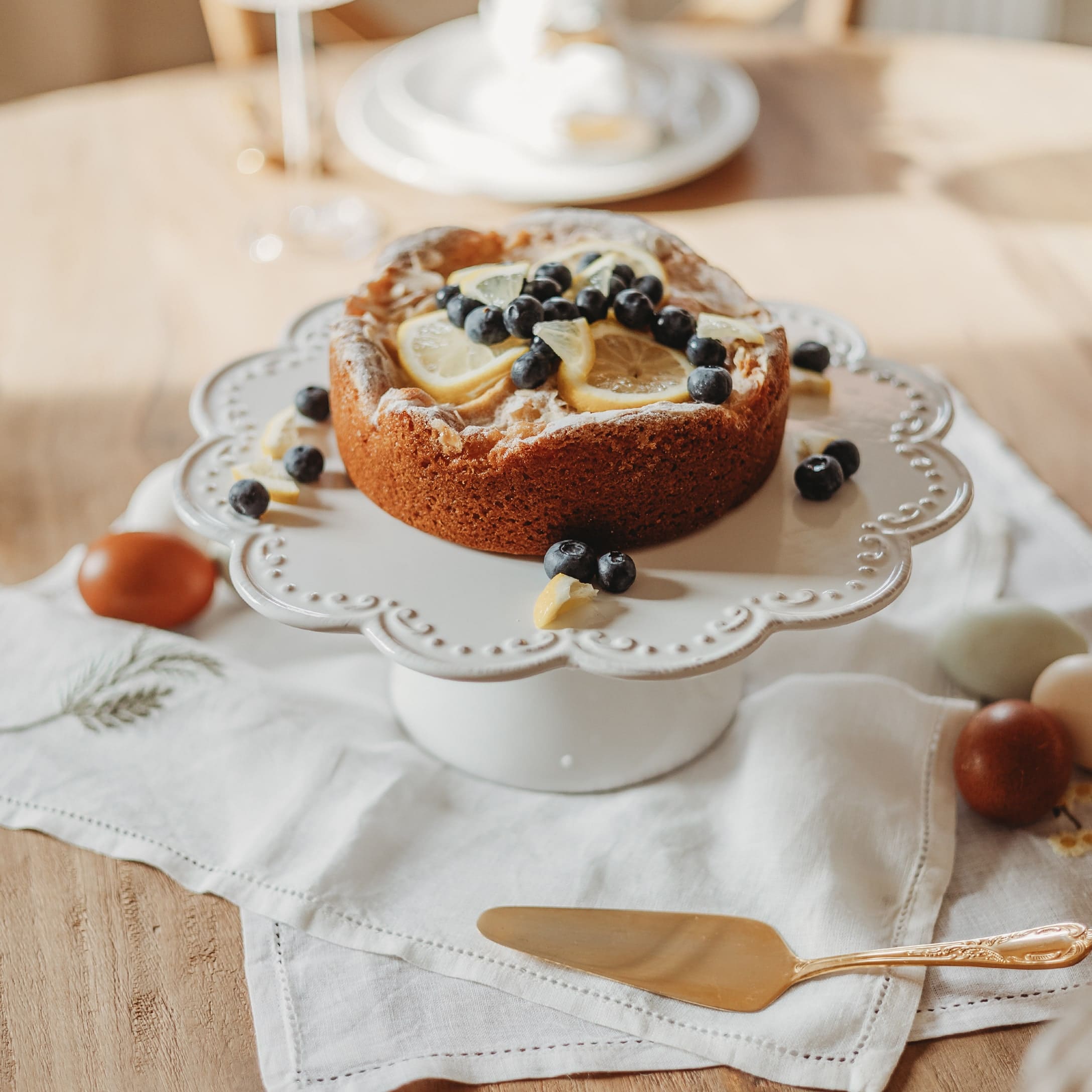 Kuchen mit Zitronenscheiben und Heidelbeeren auf weißer Keramik-Tortenplatte auf Holztisch