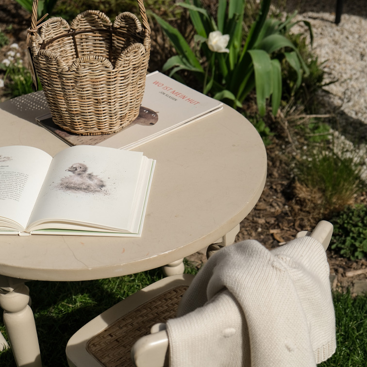 Runder beiger Gartentisch mit einem Korb aus Weide und Büchern auf dem Rasen bei Sonnenschein