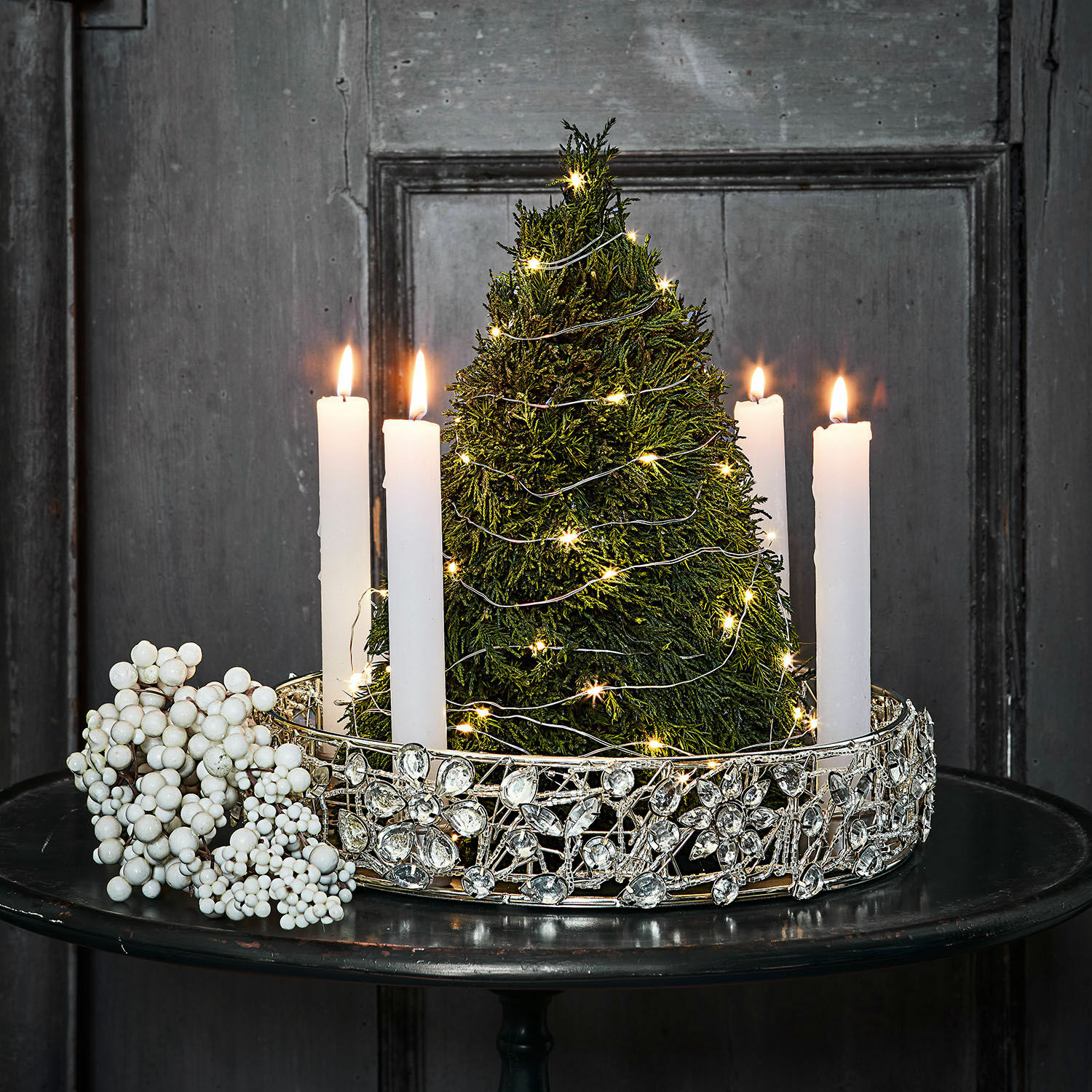 Kerzenhalter Hope Weihnachtsdeko mit grünem Baum, weißen Kerzen und silbernem Schmuckring auf schwarzem Tisch