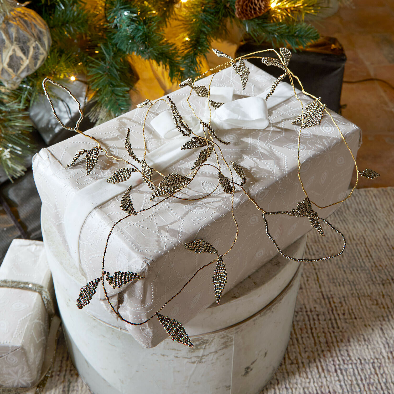 Girlande Laymira Elegantes Geschenk in weißem Papier mit feinem Muster und Metallblatt-Dekoration verpackt