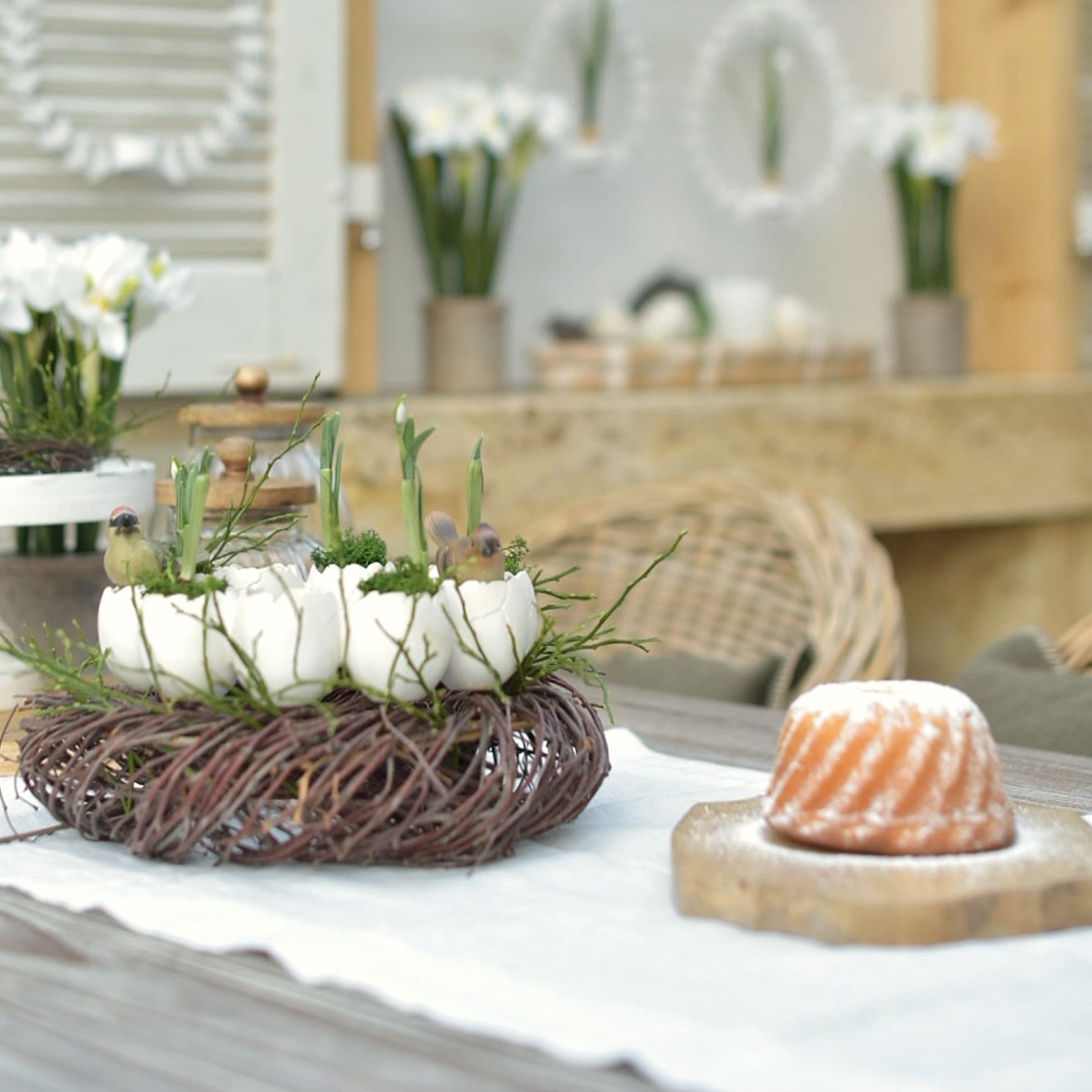 Dekorativer Kranz aus Naturzweigen mit weißen Eierschalen und grünen Pflanzen auf dem Tisch