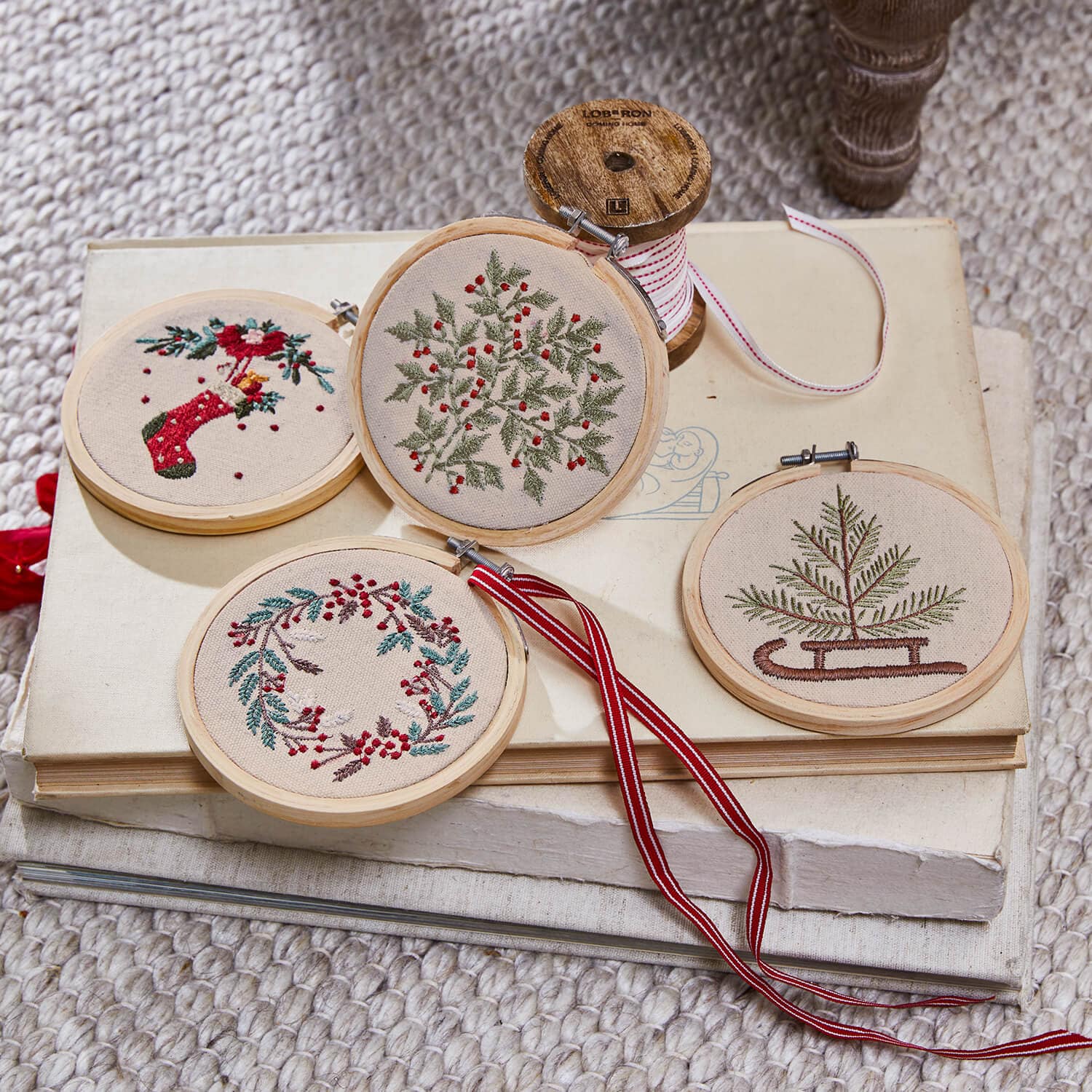 Set aus vier bestickten Weihnachtsanhängern mit pflanzlichen Motiven und roten Akzenten auf beigem Stoff
