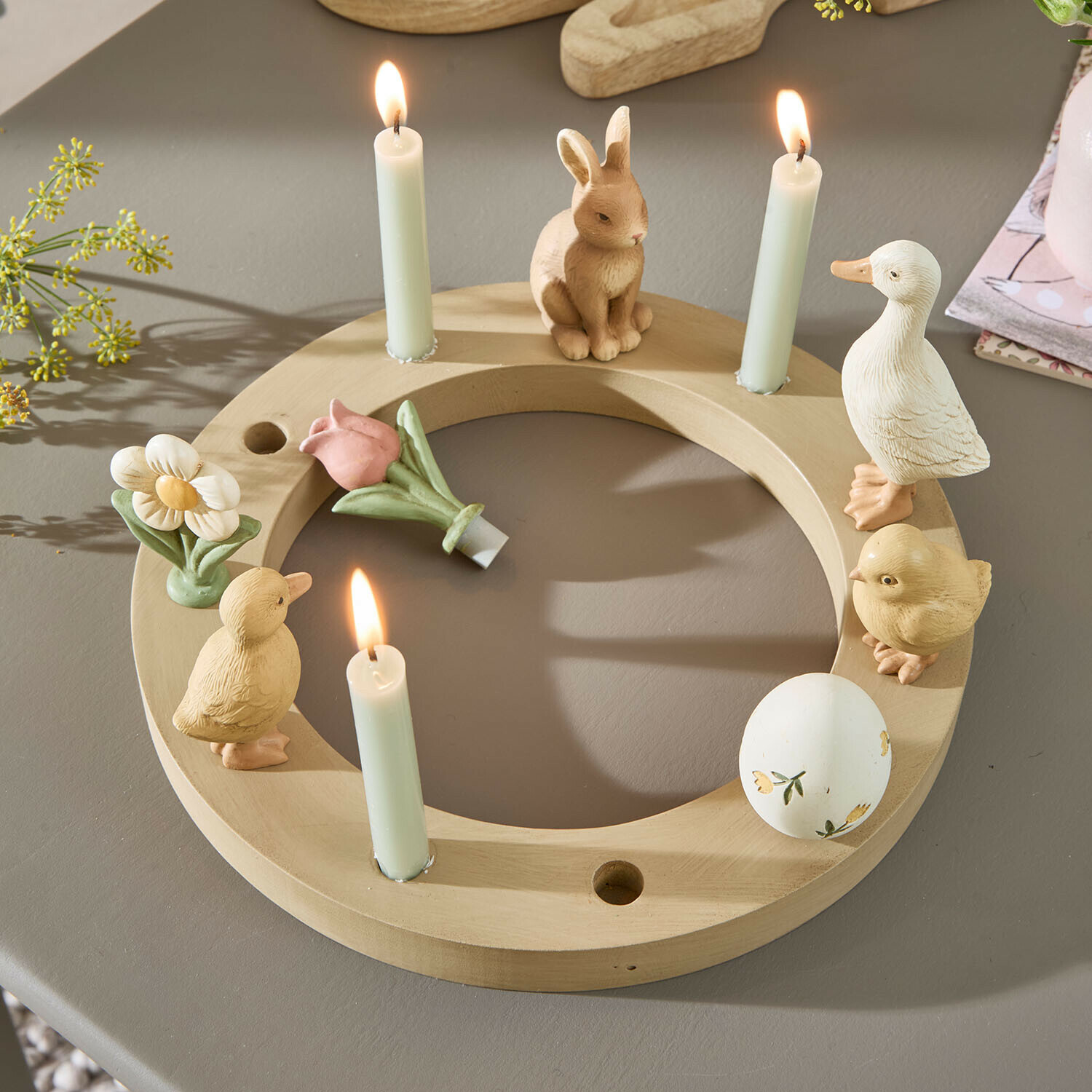 Runder Holz-Kerzenhalter mit Hasen-, Enten- und Blumenfiguren sowie drei weißen brennenden Kerzen
