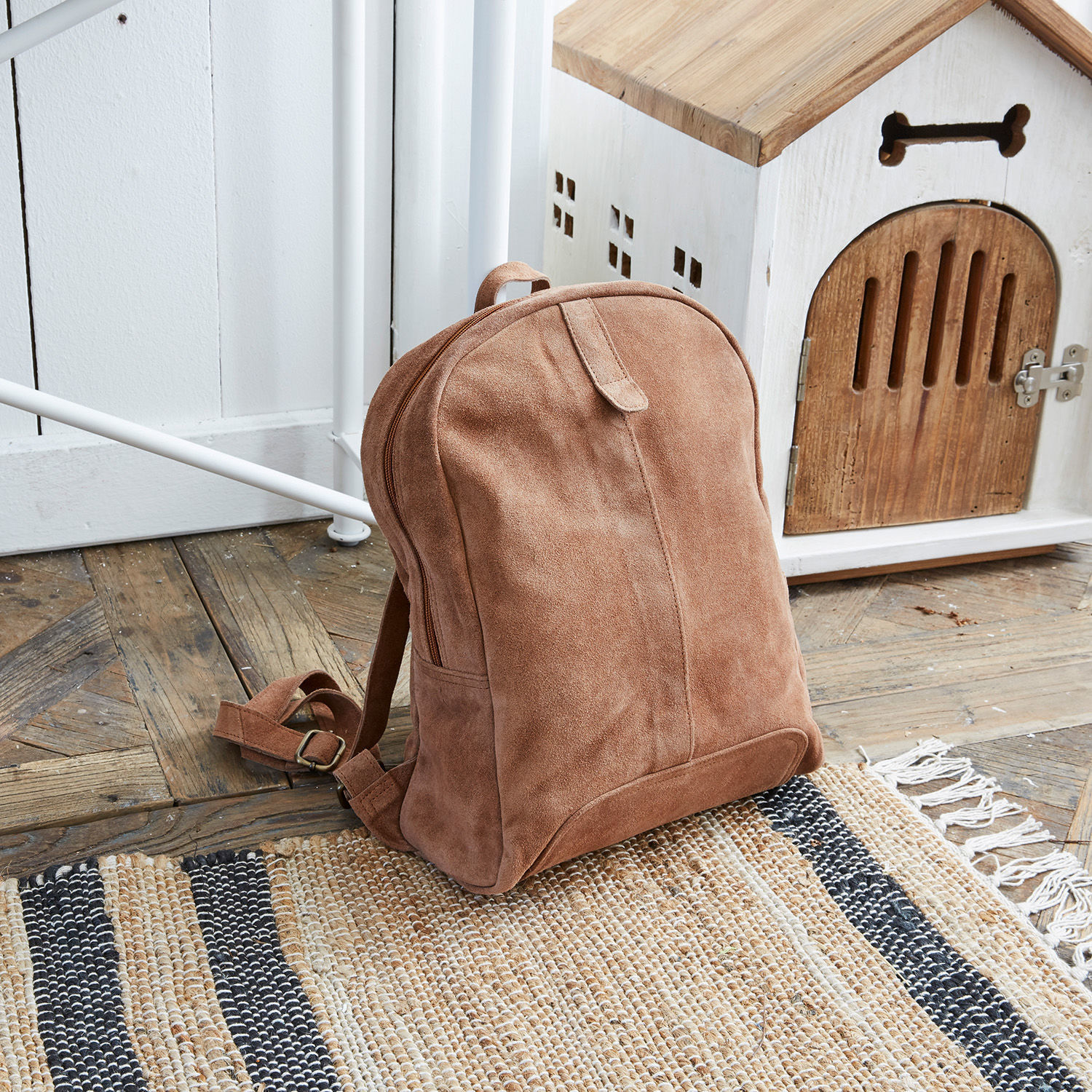 Rucksack Palau Brauner Rucksack aus Wildleder auf Holzboden neben weißem Hundehäuschen aus Holz