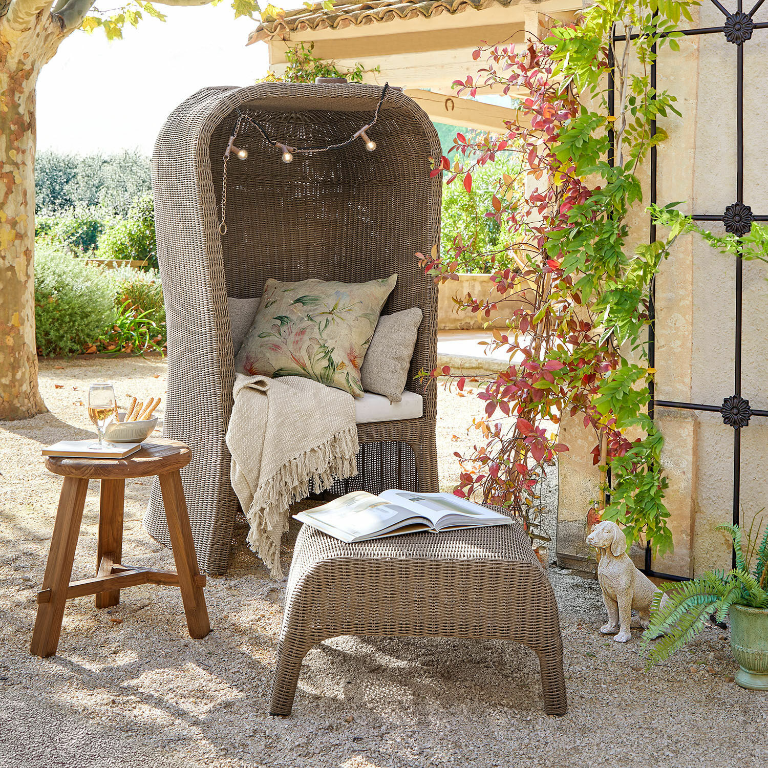 Strandkorb mit Hocker Sanivane Grauer Rattan-Sessel mit Kissen und Decke, Holztisch und Hocker mit Buch im Garten