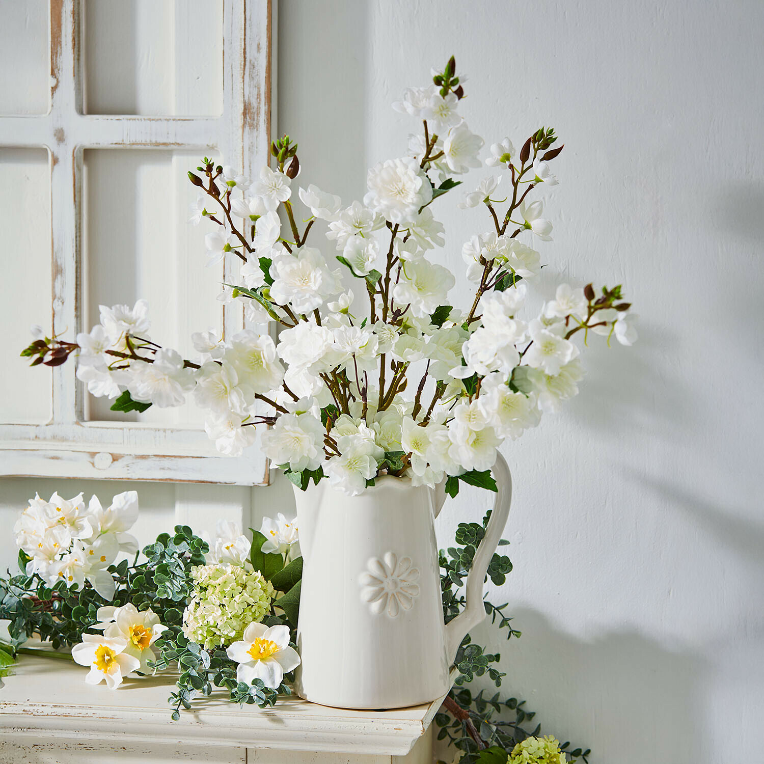 Weißer Keramikkrug mit Blumenrelief und weißen dekorativen Blütenzweigen