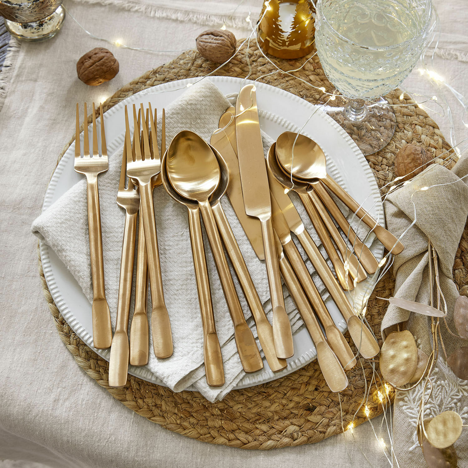Besteck Malroy Set goldfarbener Edelstahl-Bestecke auf weißem Teller mit festlicher Dekoration und LED-Lichterkette