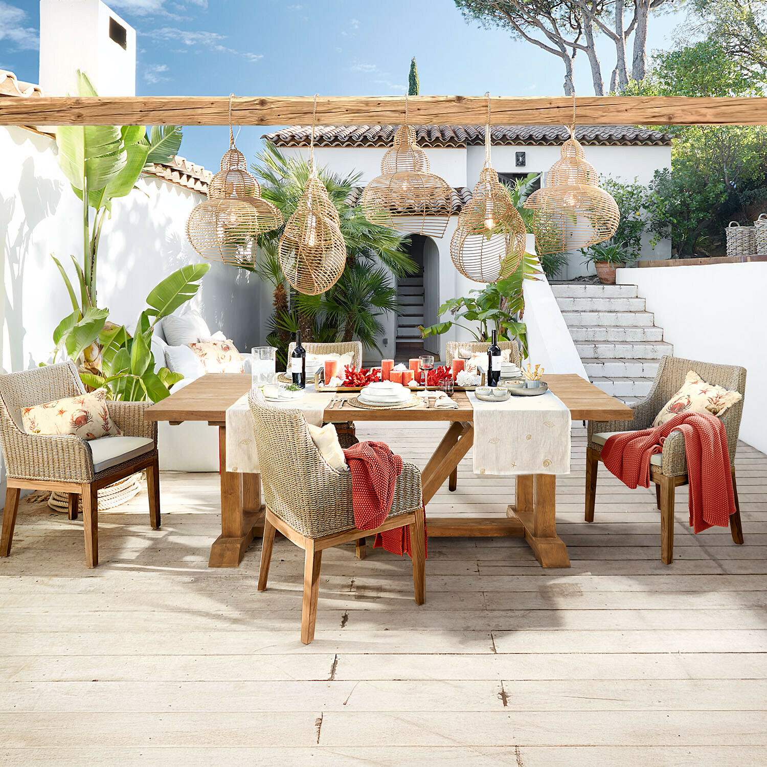 Tisch Melvoro Gartenmöbel-Set aus Holz und Rattan in Naturtönen mit hängenden Korblampen auf Terrasse