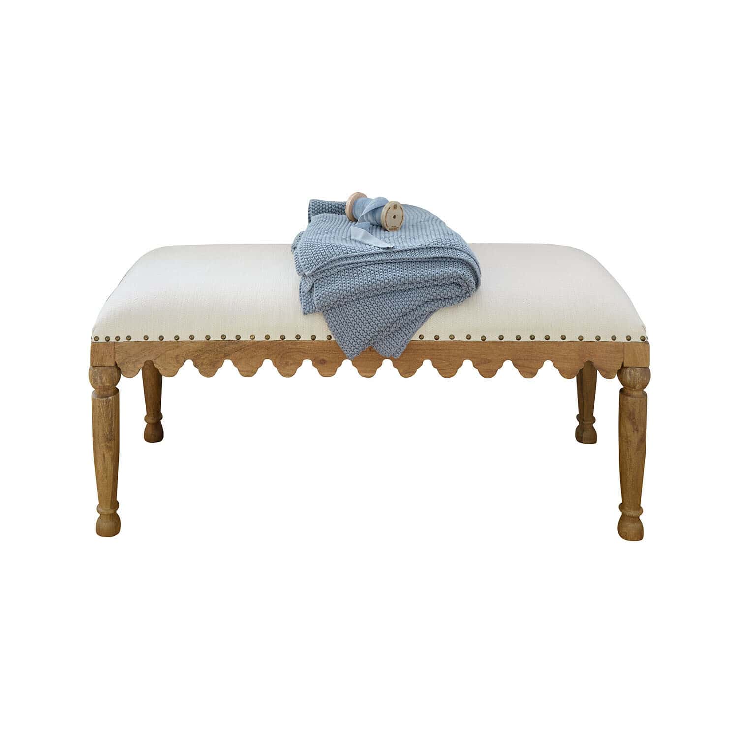 Gepolsterte Bank mit hellem Stoff und Holzrahmen, darüber ein blau gestrickter Überwurf
