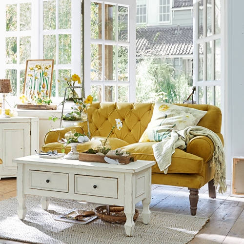 Gelbes Samtsofa im Vintage-Stil in hellem Wohnzimmer mit weißem Holztisch und Dekorationen