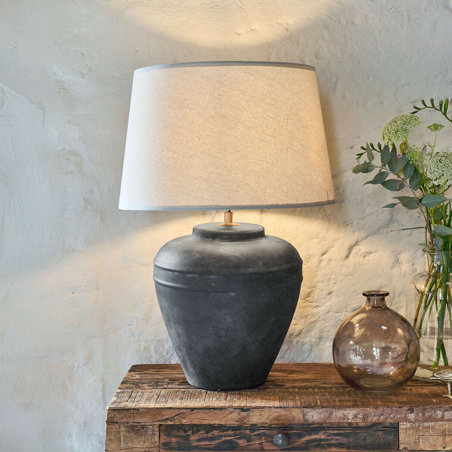 Tischlampe aus schwarzer Keramik mit beigem Lampenschirm auf rustikalem Holztisch
