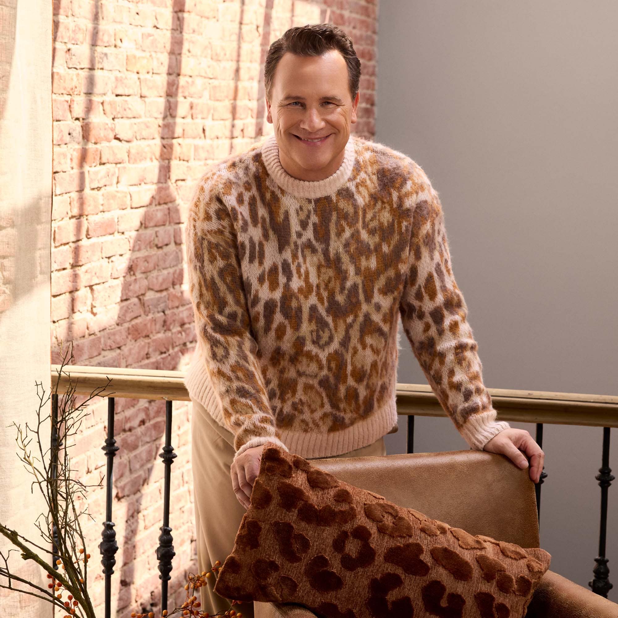 Mann in weichem Pullover mit braunem Leopardenmuster vor Ziegelwand sitzend