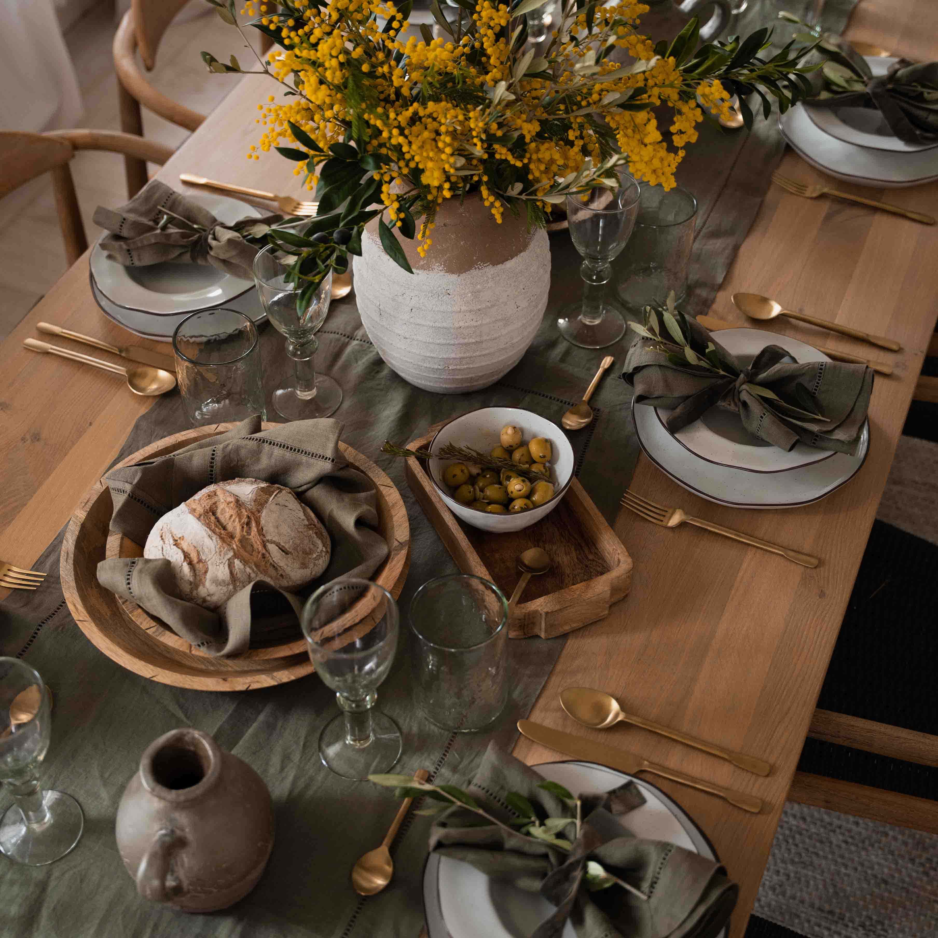 Rustikaler Holztisch mit weißem Geschirr, grünen Servietten und gelbem Blumenstrauß in Tonvase