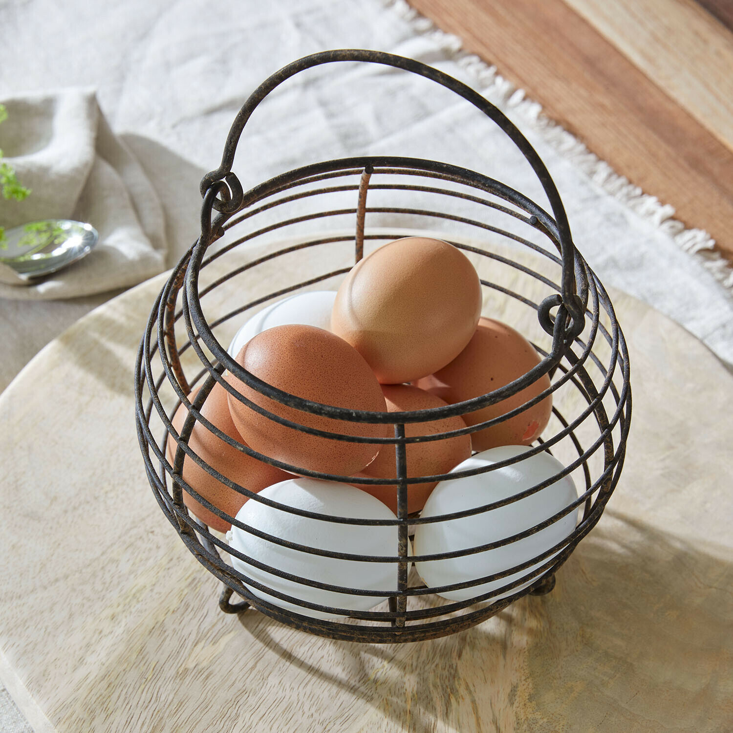 Vintage Metall-Eierkorb mit braunen und weißen Eiern auf hellem Holzuntergrund