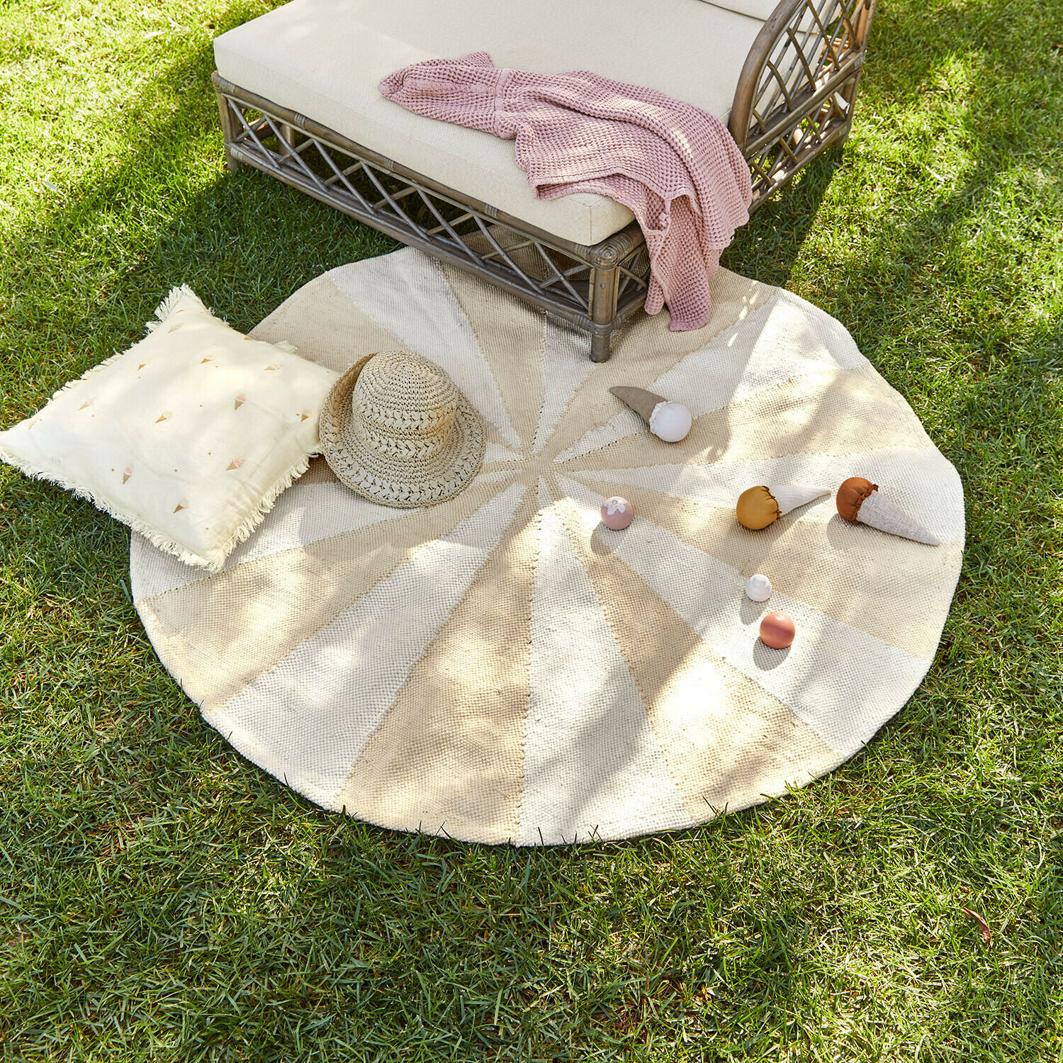 Runder Teppich aus Naturmaterial in Beige-Creme-Tönen auf Gras mit Kissen und Strohhut