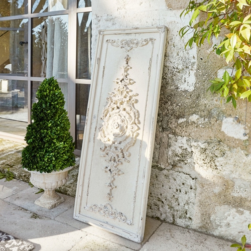 Weißes dekoratives Holzpaneel mit Vintage-Relief vor einer Steinmauer neben einer grünen Pflanze