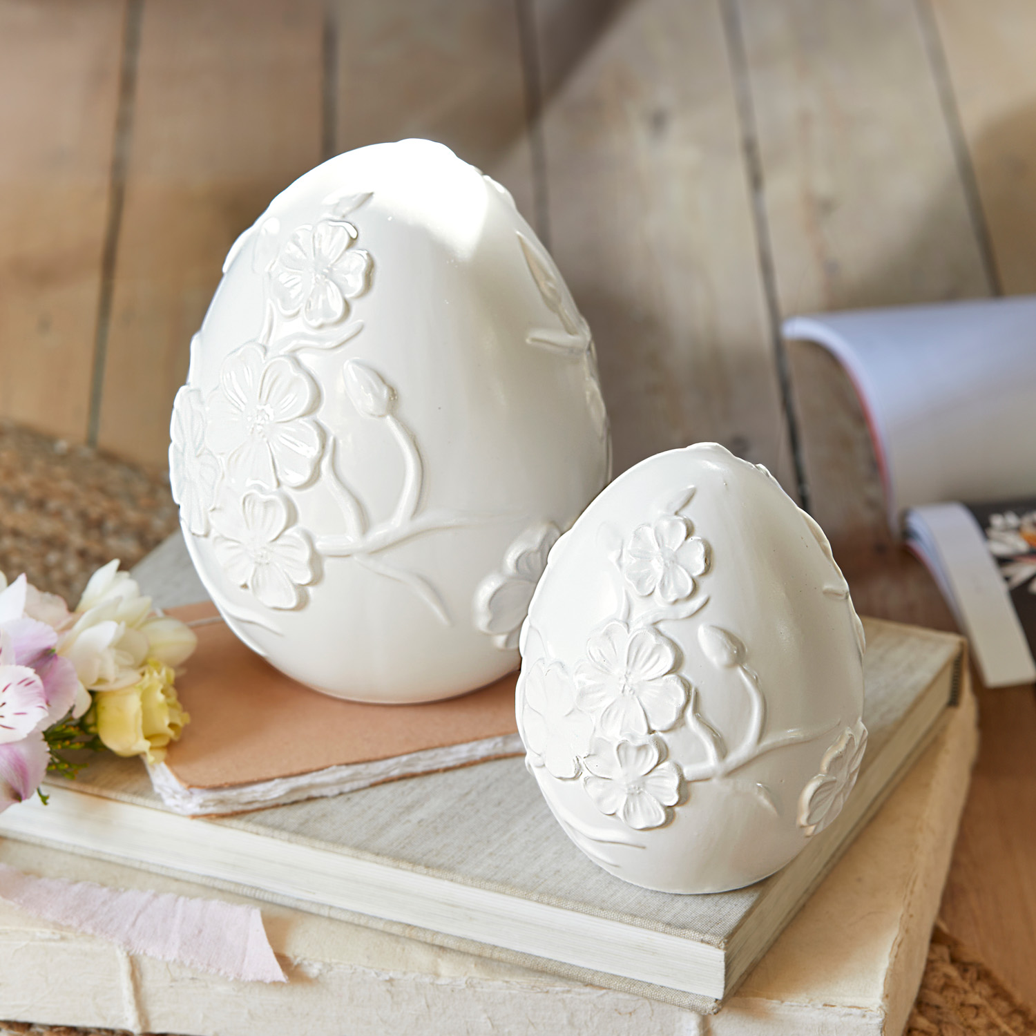 Weiße Keramik-Eier mit floralem Relief auf Büchern, dekorative Frühlingsdekoration