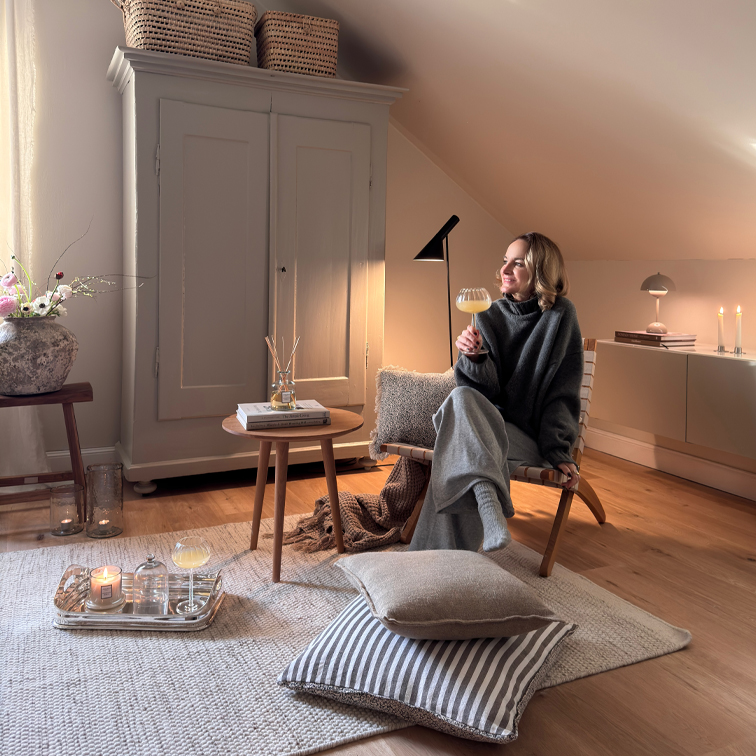 Gemütliche Sitzecke mit Holzstuhl, grauer Decke und Kerzen auf hellem Teppich
