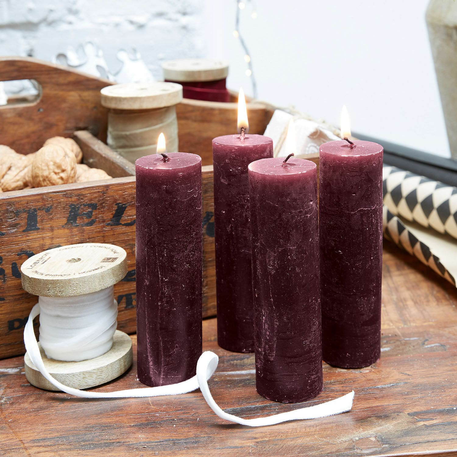 Kerze 4er Set Muriel Vier bordeauxfarbene Wachskerzen auf Holztisch mit Dekoband und Walnüssen