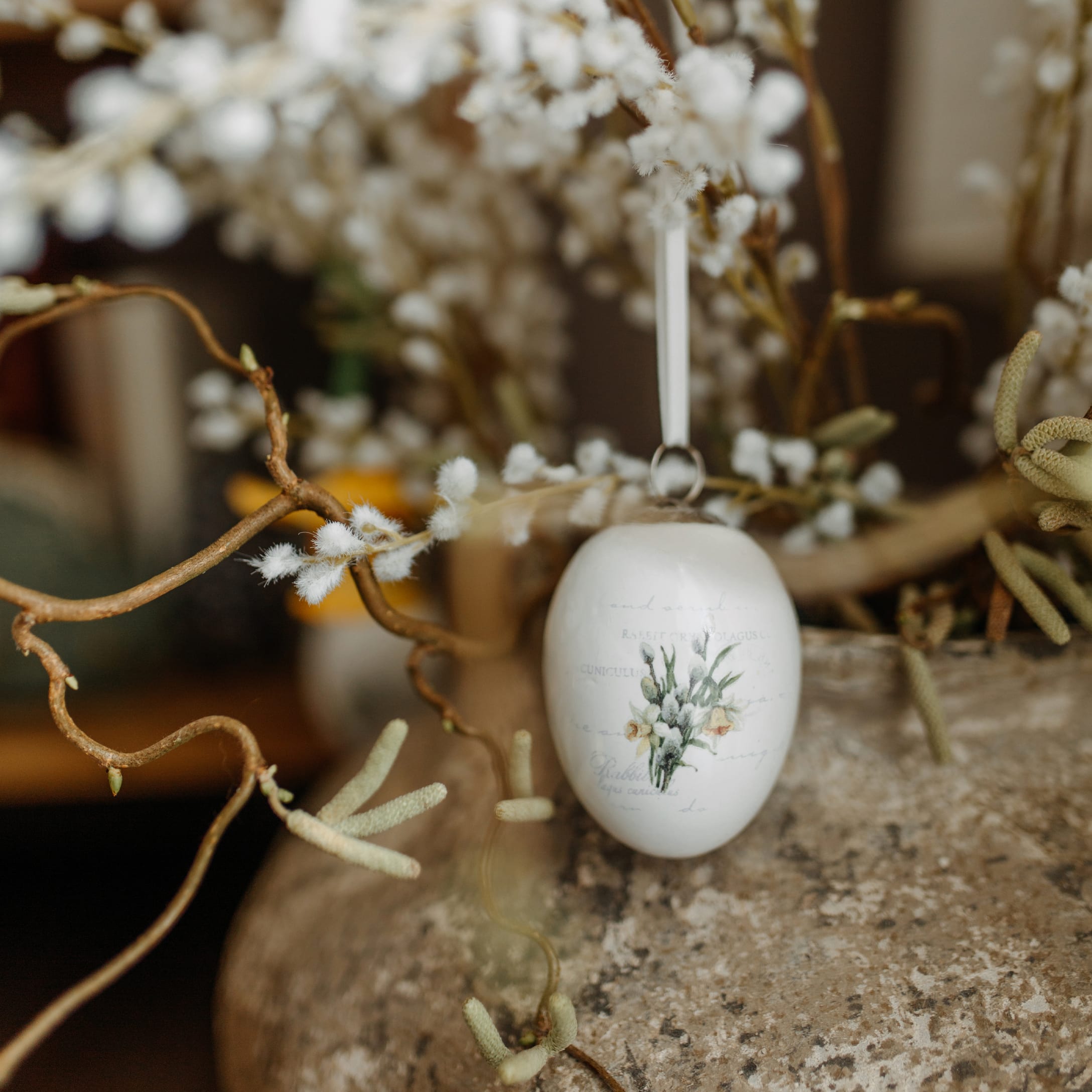 Weiße Keramik-Ostereier-Dekoration mit Blumenmotiv an dekorativem Zweig hängend