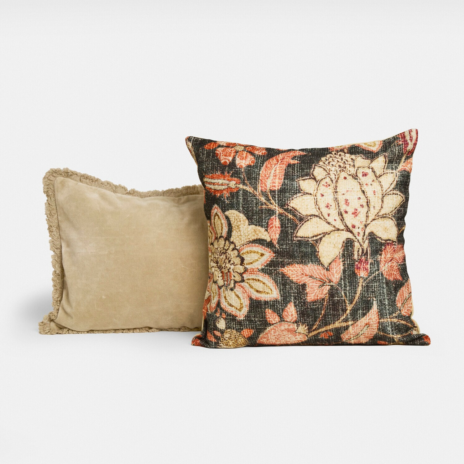 Set aus zwei dekorativen Kissen, eines beige mit Fransen, das andere mit floralem Muster auf dunklem Hintergrund