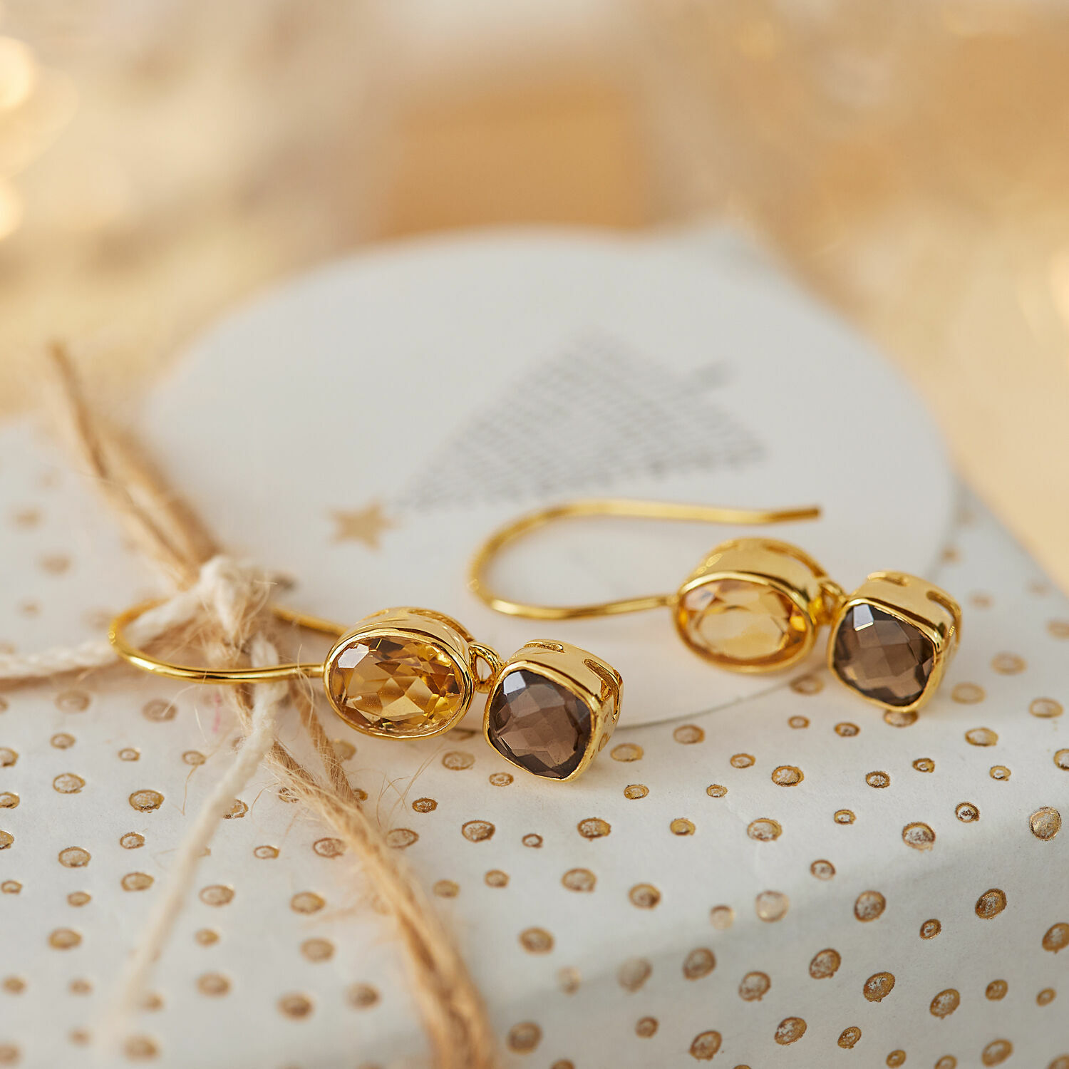 Ohrringe Ovique Goldene Ohrringe mit facettierten braunen Steinen auf dekorativem Geschenkpapier