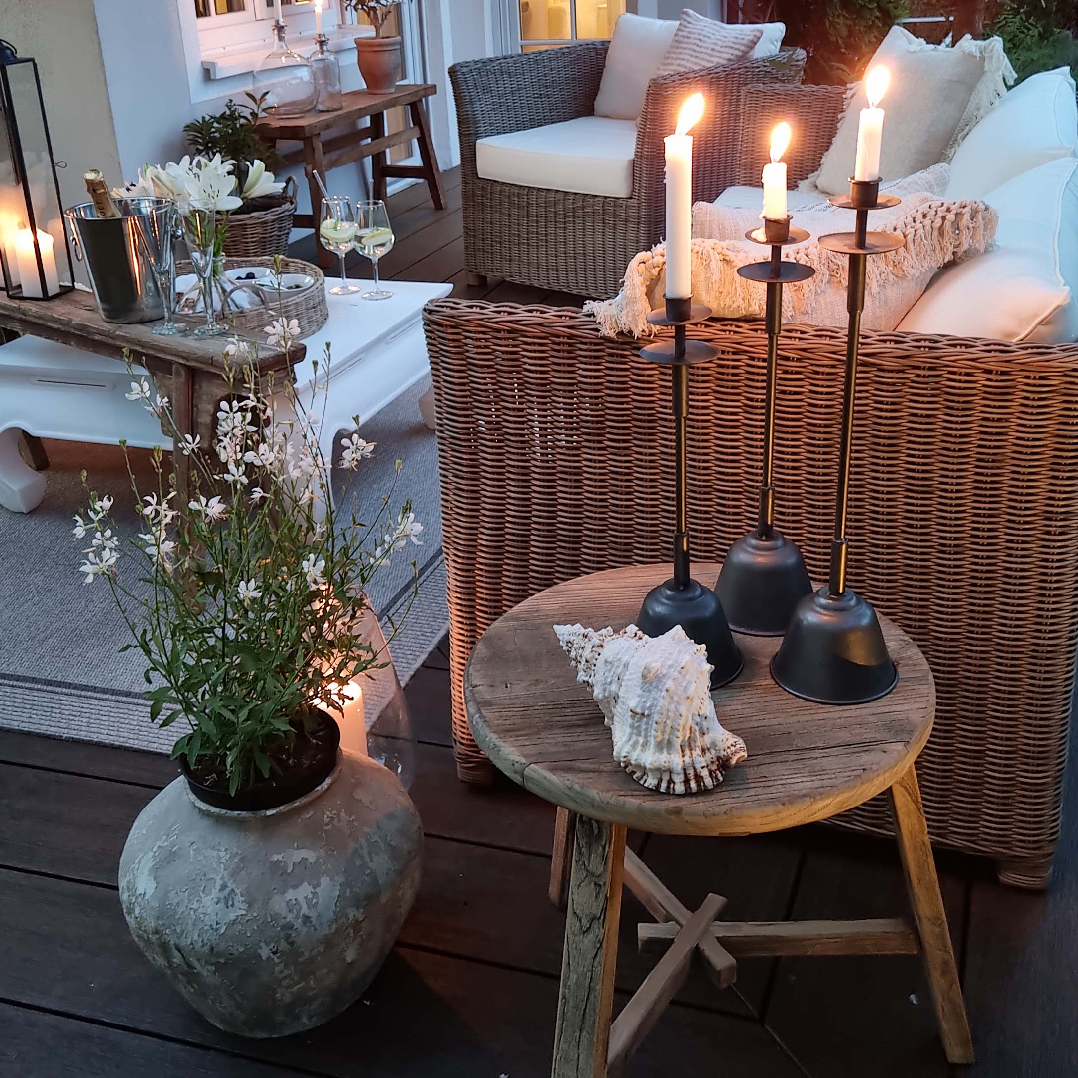 Gemütliche Terrasse mit Rattansofa, Holztisch und schwarzen Metallkerzenhaltern mit weißen Kerzen