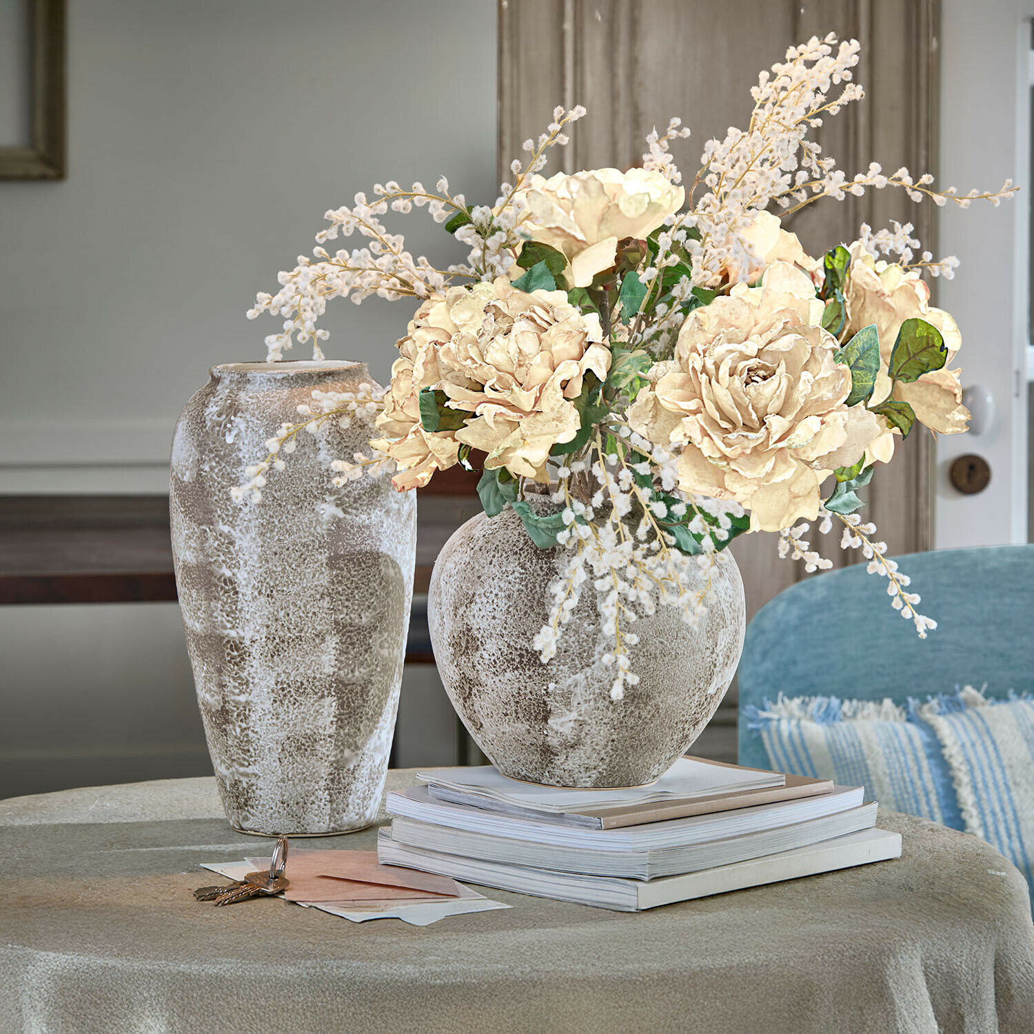 Dekorativer Keramikvase in Beige-Braun mit cremefarbenem Blumenstrauß auf Tisch mit gestapelten Büchern