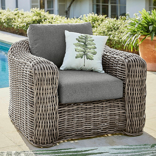 Grau geflochtener Gartensessel mit grauen Polstern und dekorativem Kissen mit Blattmotiv