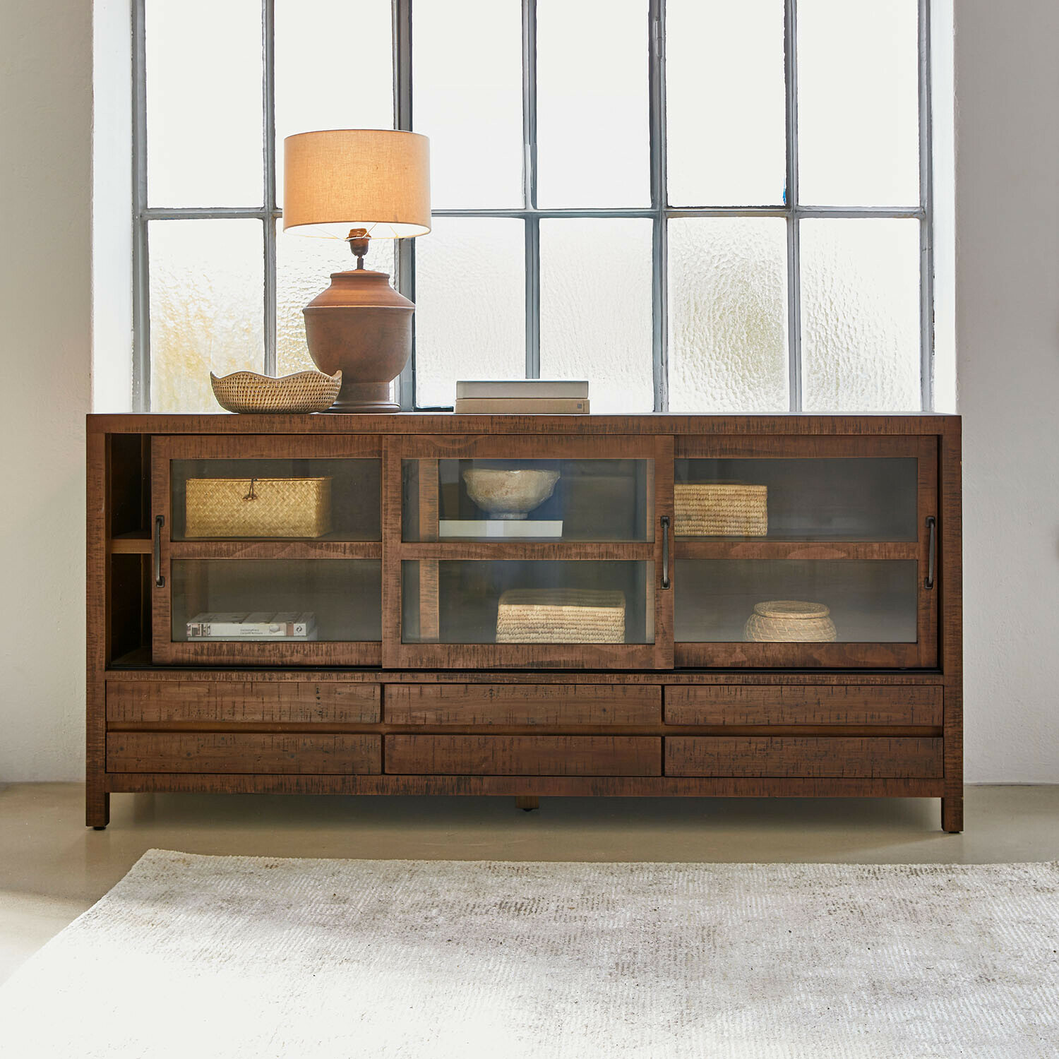 Holzkommode mit Glastüren und Schubladen, dekoriert mit Lampe und geflochtenen Körben