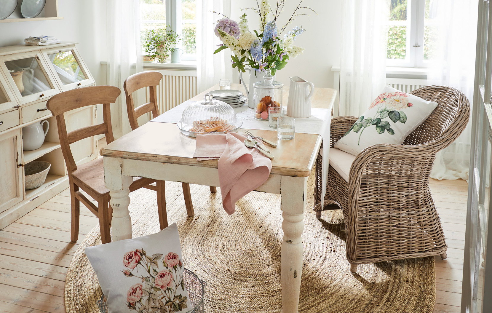 Shabby Chic Esszimmer mit Holztisch, Rattansessel und Blumenarrangement in hellem Raum