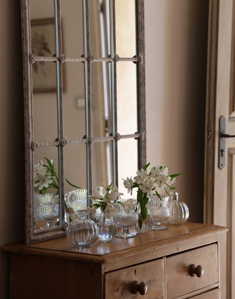 Holzkommode mit Metallrahmen-Spiegel und Glasvasen mit weißen Blumen im Vintage-Stil
