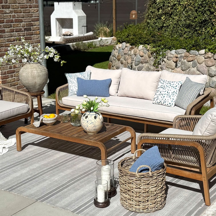 Gartenmöbel-Set mit Holztisch und beige Sofa mit blauen gemusterten Kissen auf gestreiftem Teppich