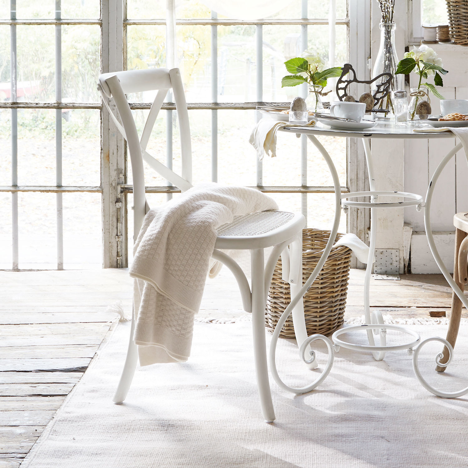 Weißer Holzstuhl mit X-förmiger Rückenlehne und geflochtenem Sitz, cremefarbene Decke darauf gelegt