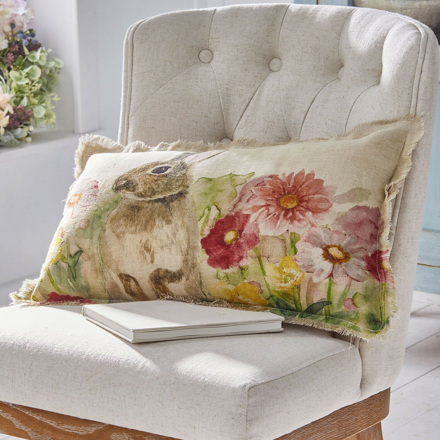 Langer Leinenkissenbezug mit Hasen- und Blumenmotiv in Pastellfarben auf hellem Stuhl