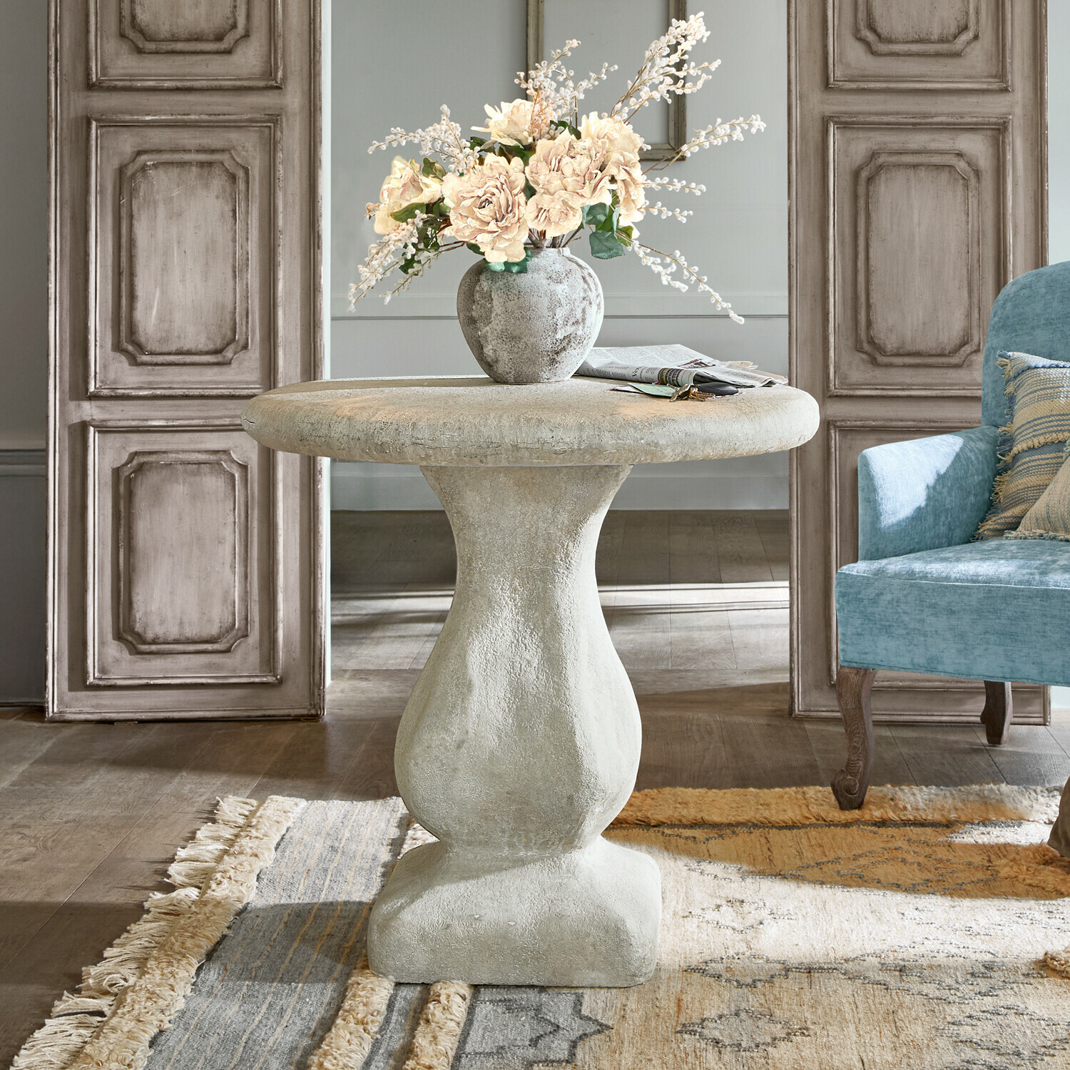 Runder grauer Betontisch mit Vase und Blumen in Wohnzimmer mit blauem Sessel