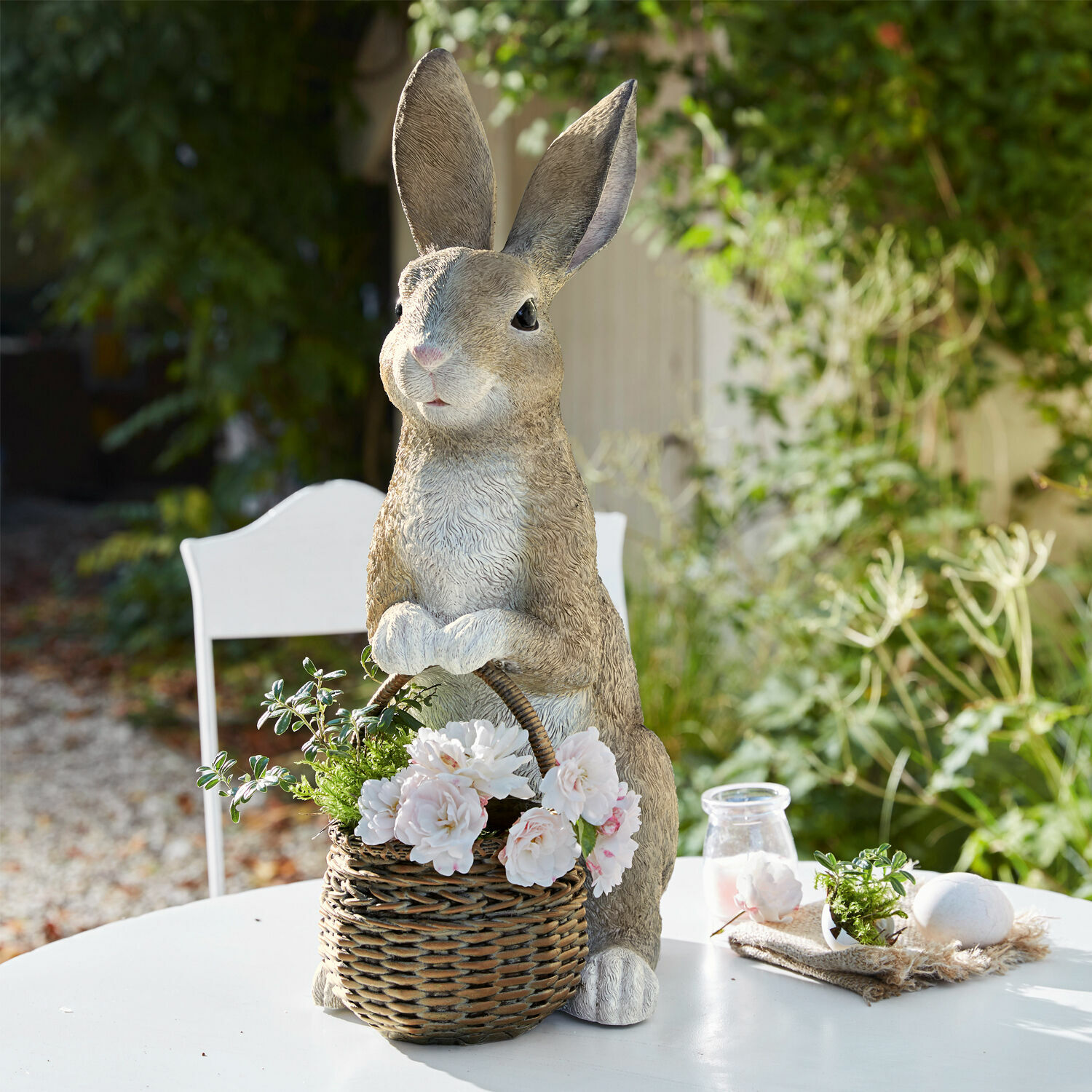 Hase mit Pflanzkorb Alais Dekorativer Kaninchen aus Kunststoff mit Weidenkorb und weißen Blumen auf Gartentisch