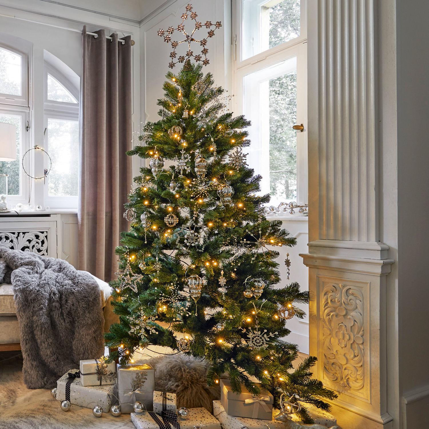Weihnachtsbaum mit grünen Zweigen und silbernen Dekorationen im hellen Wohnzimmer mit Geschenken
