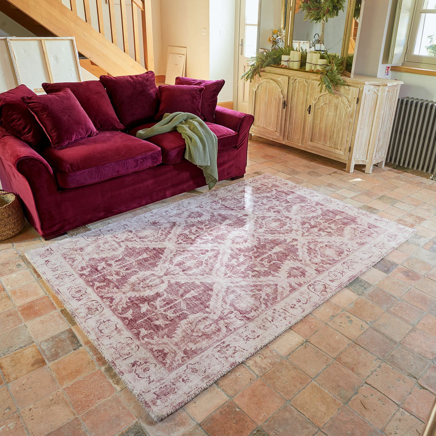 Teppich Mirellis Rotes Samsofa mit Kissen und grünem Plaid auf Vintage-Teppich in gemütlichem Wohnzimmer