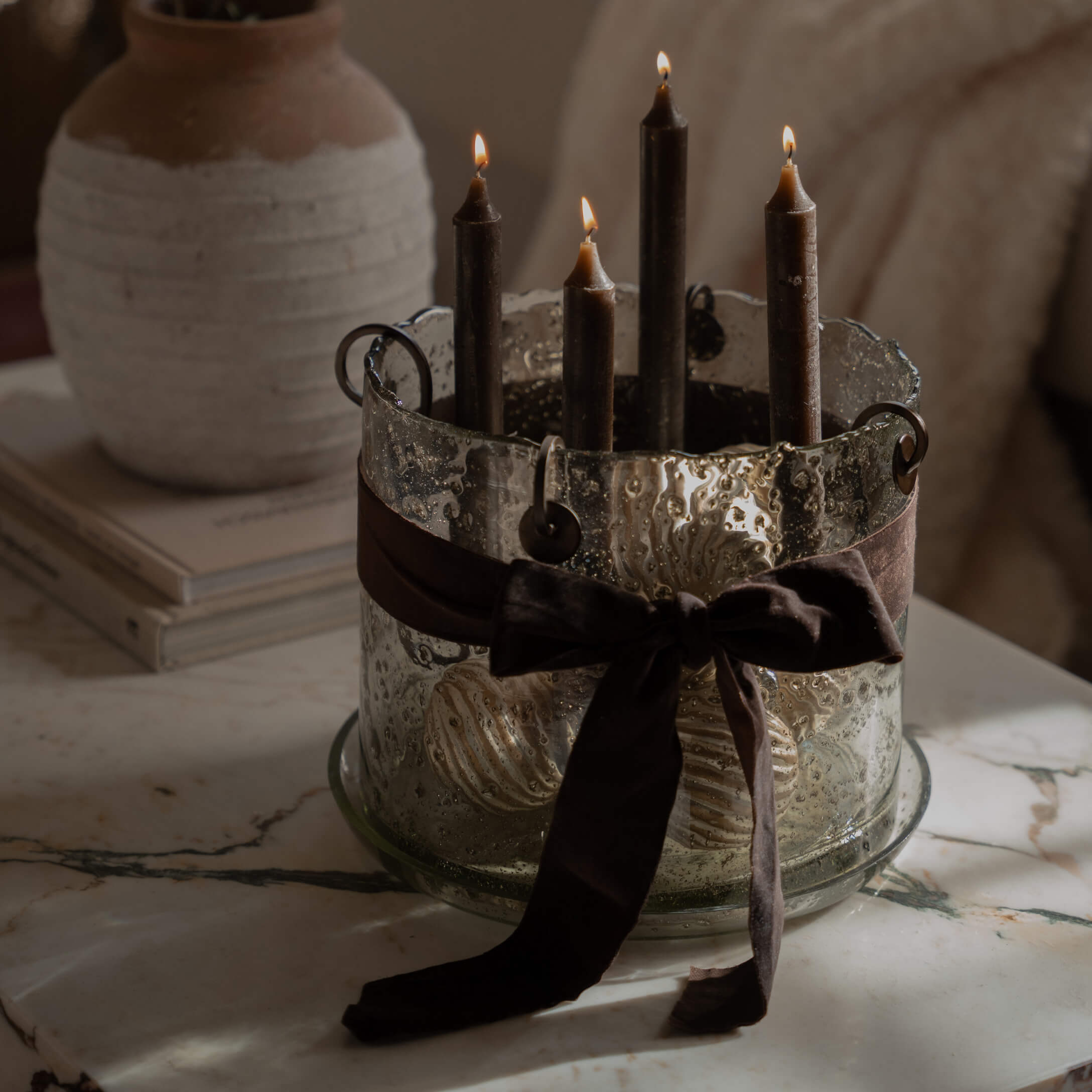Glas-Kerzenhalter mit vier schwarzen Kerzen und brauner Schleife auf Marmorplatte