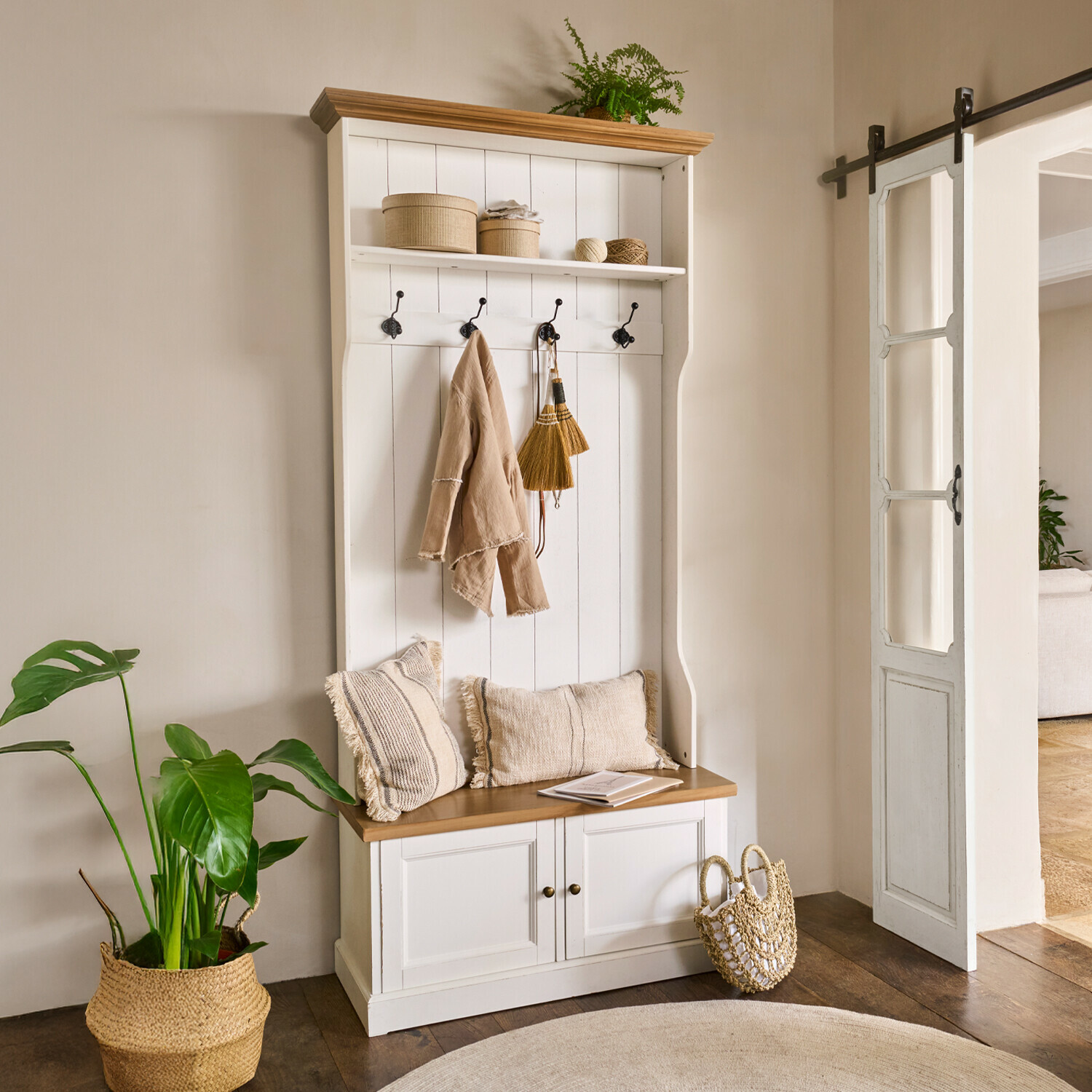 Weiße Holzgarderobe mit Sitzbank, Haken, beigen Kissen und natürlichen Dekoelementen im Flur